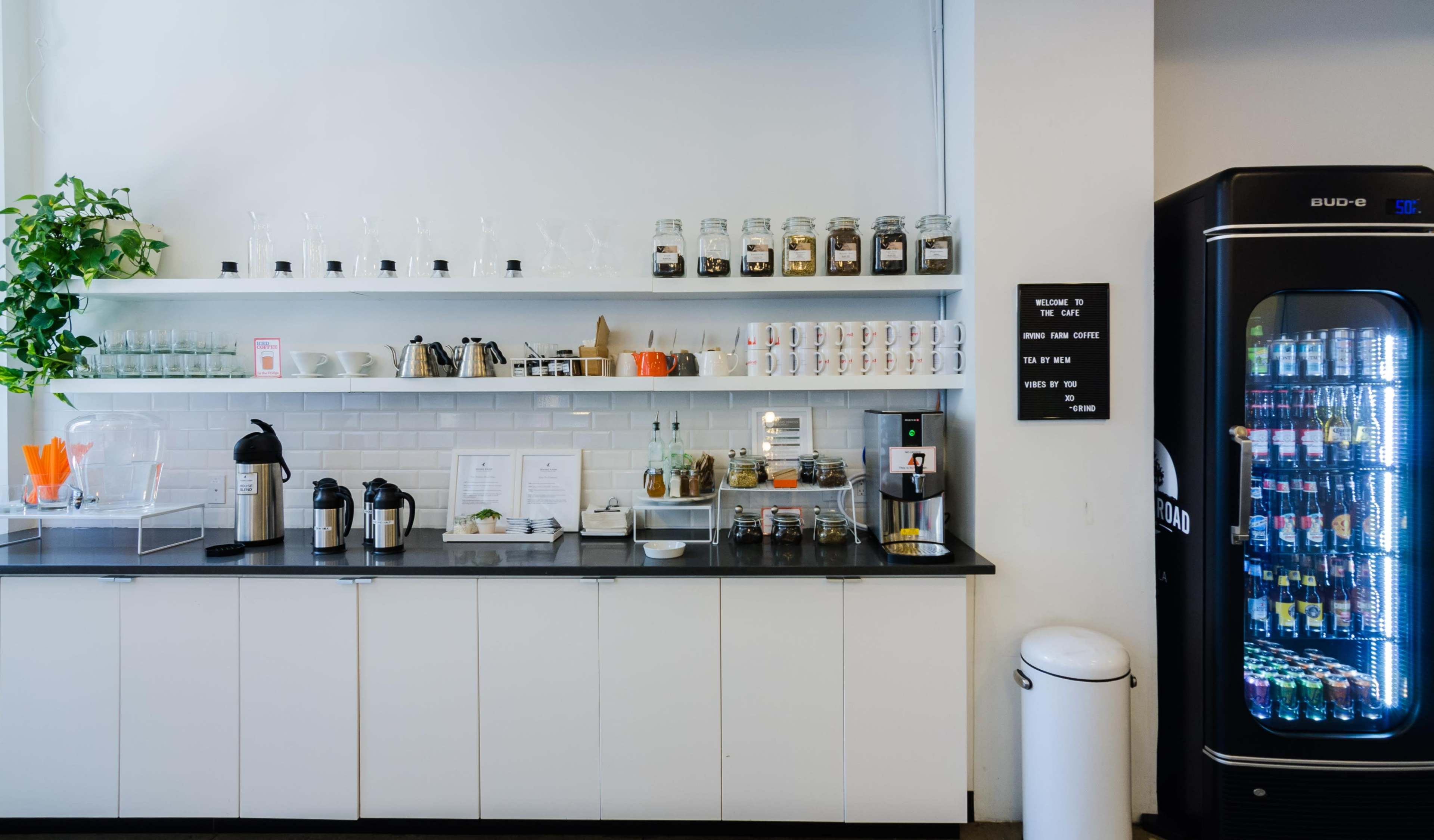 A clean café interior featuring a counter with glass containers, coffee dispensers, and a vending machine against a white wall.