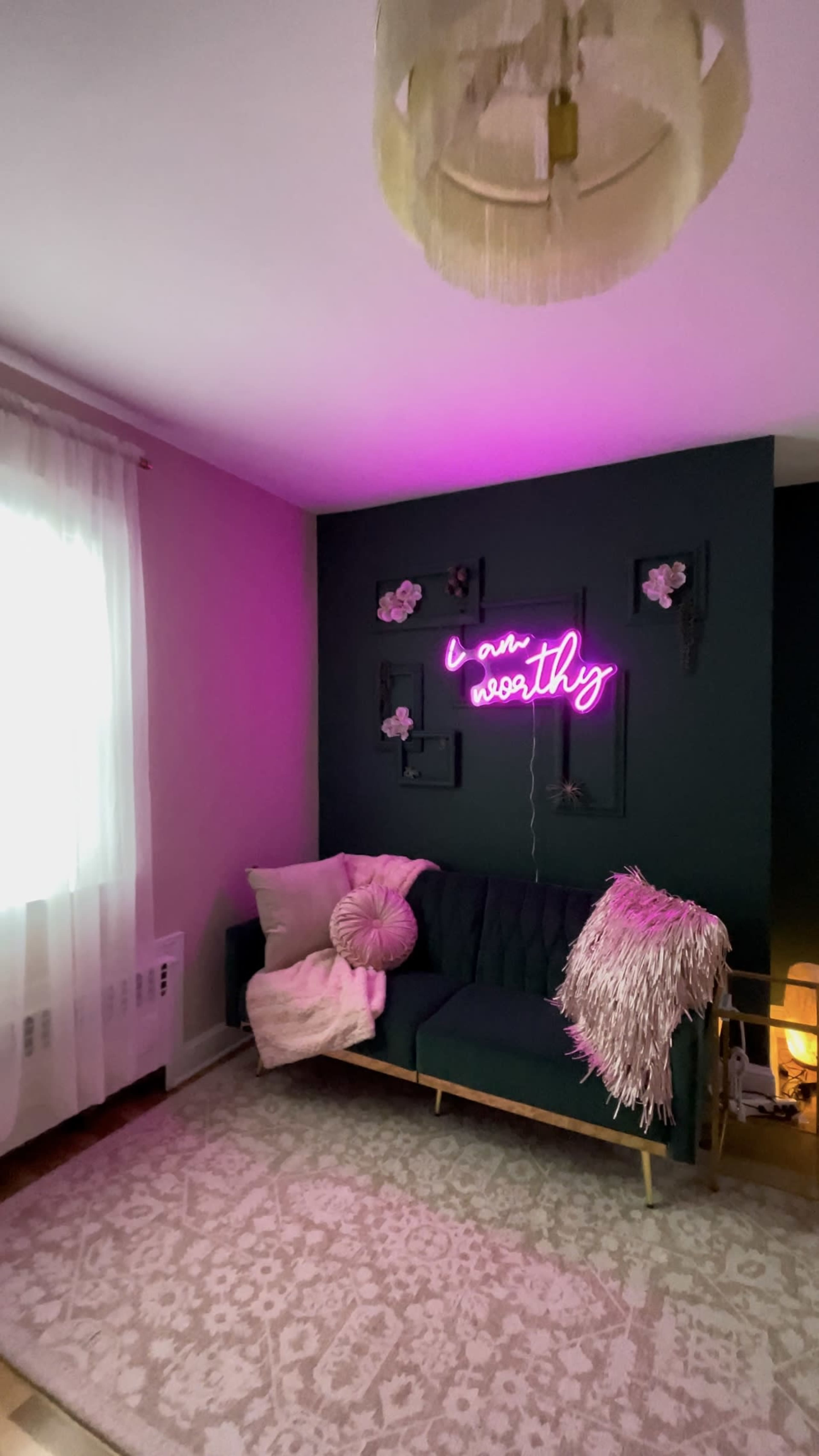 The image shows a cozy living room with a green accent wall featuring a neon sign, a tufted couch, and soft curtains.