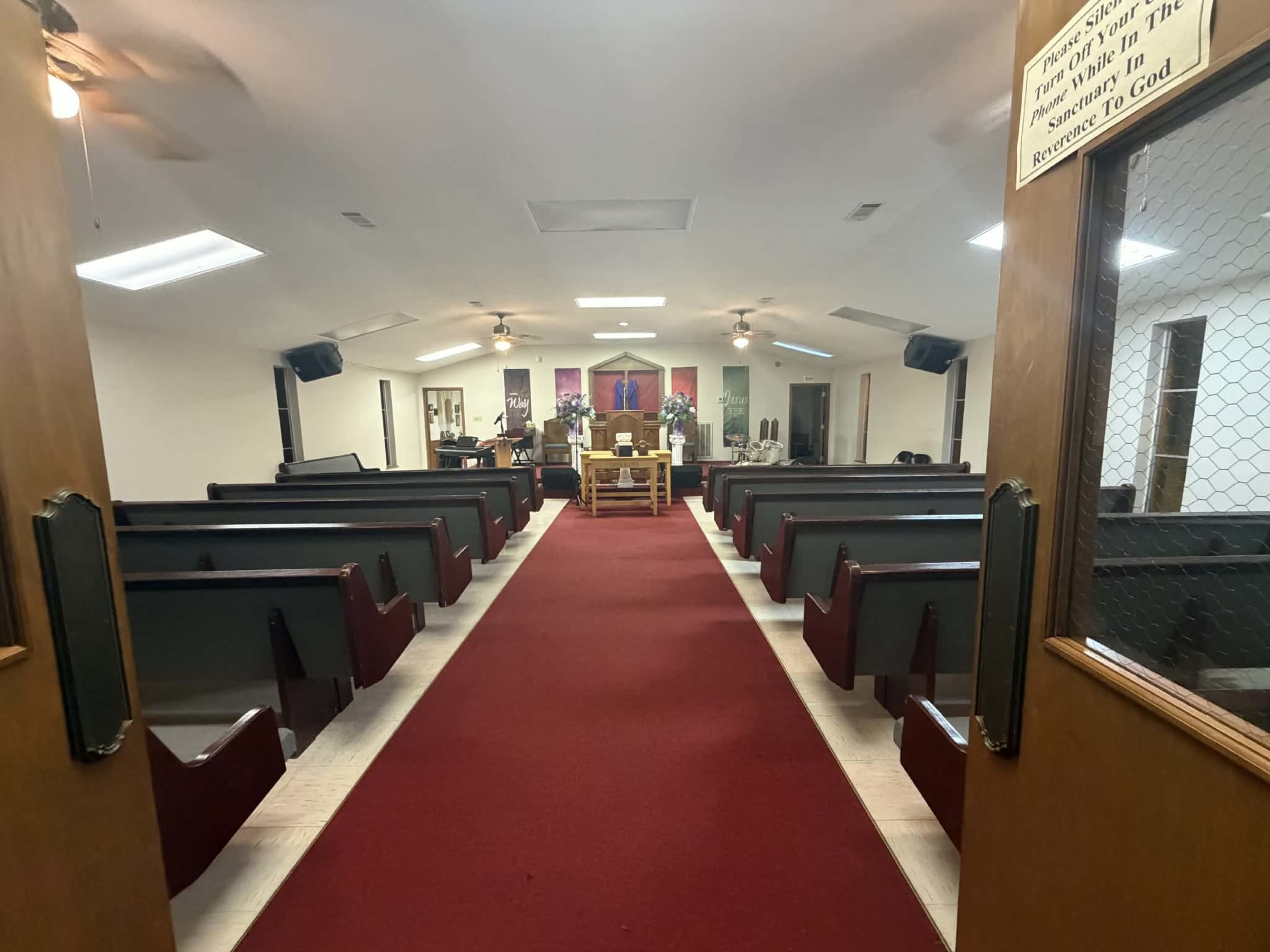 The image shows the interior of a church with a red carpet aisle leading to an altar, surrounded by wooden pews on both sides.