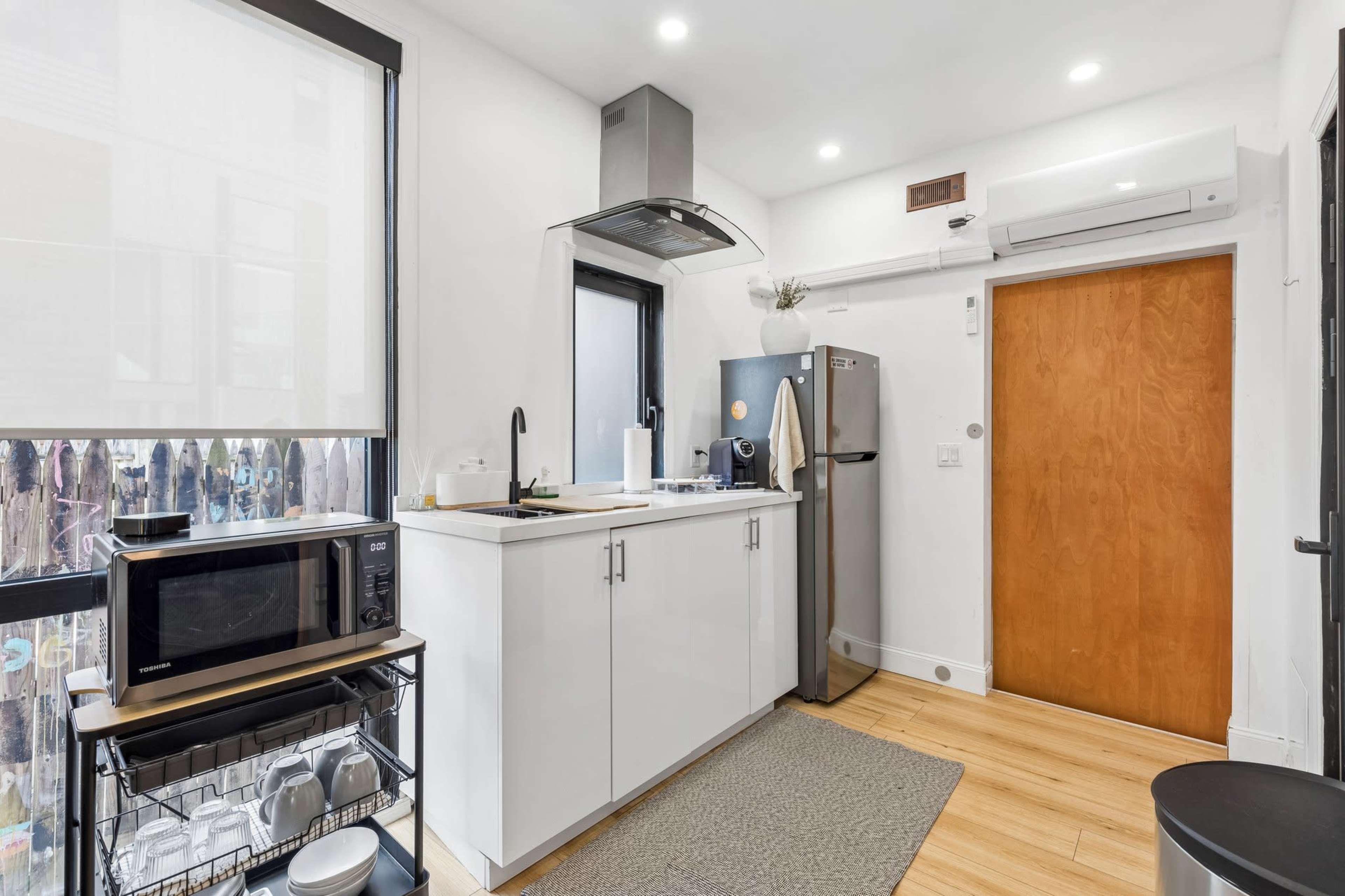 The image shows a modern kitchen with white cabinets, a stainless steel refrigerator, a microwave, and wood flooring.