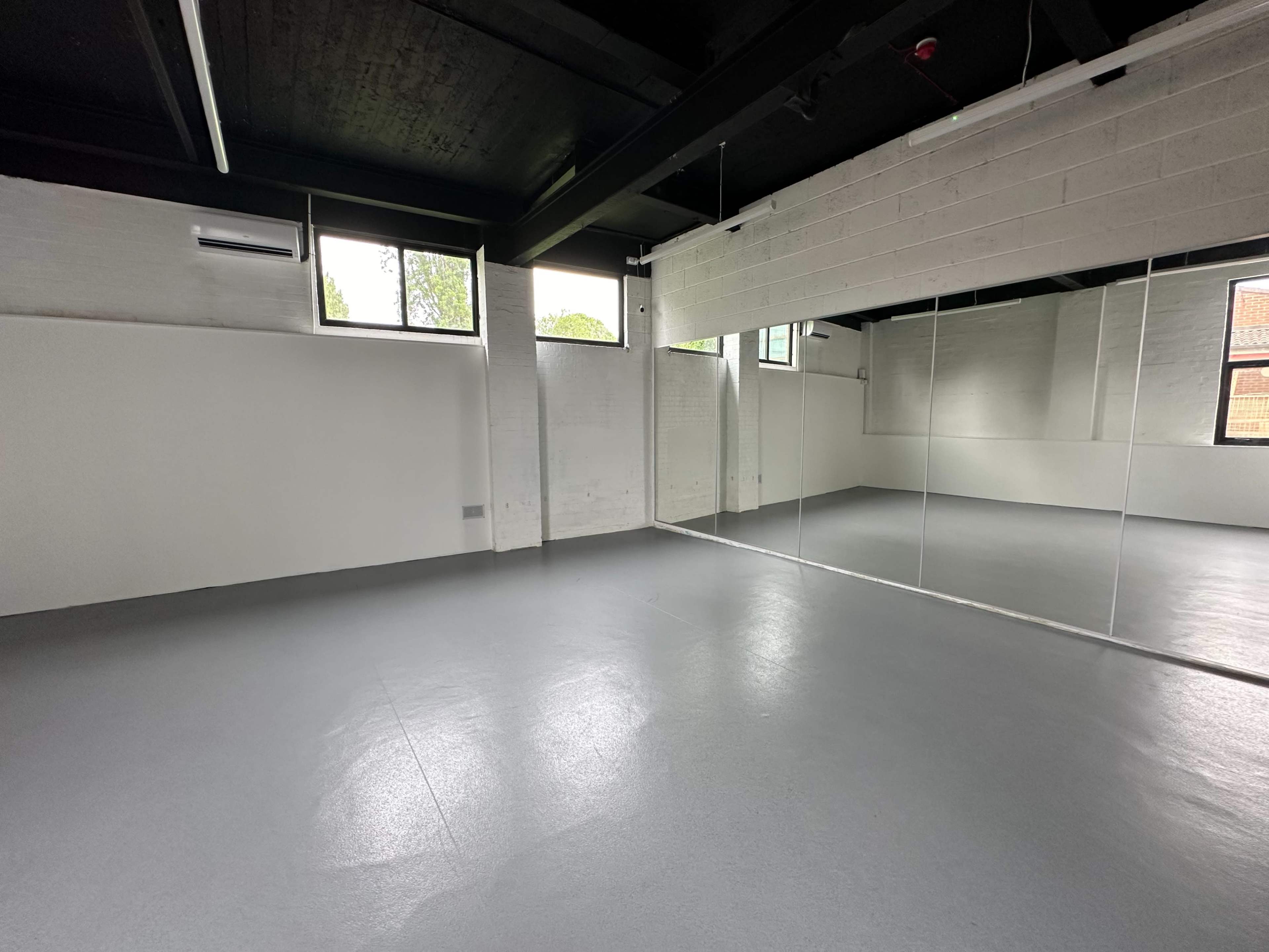 A spacious, empty room with gray flooring, white walls, and large mirrors along one side.