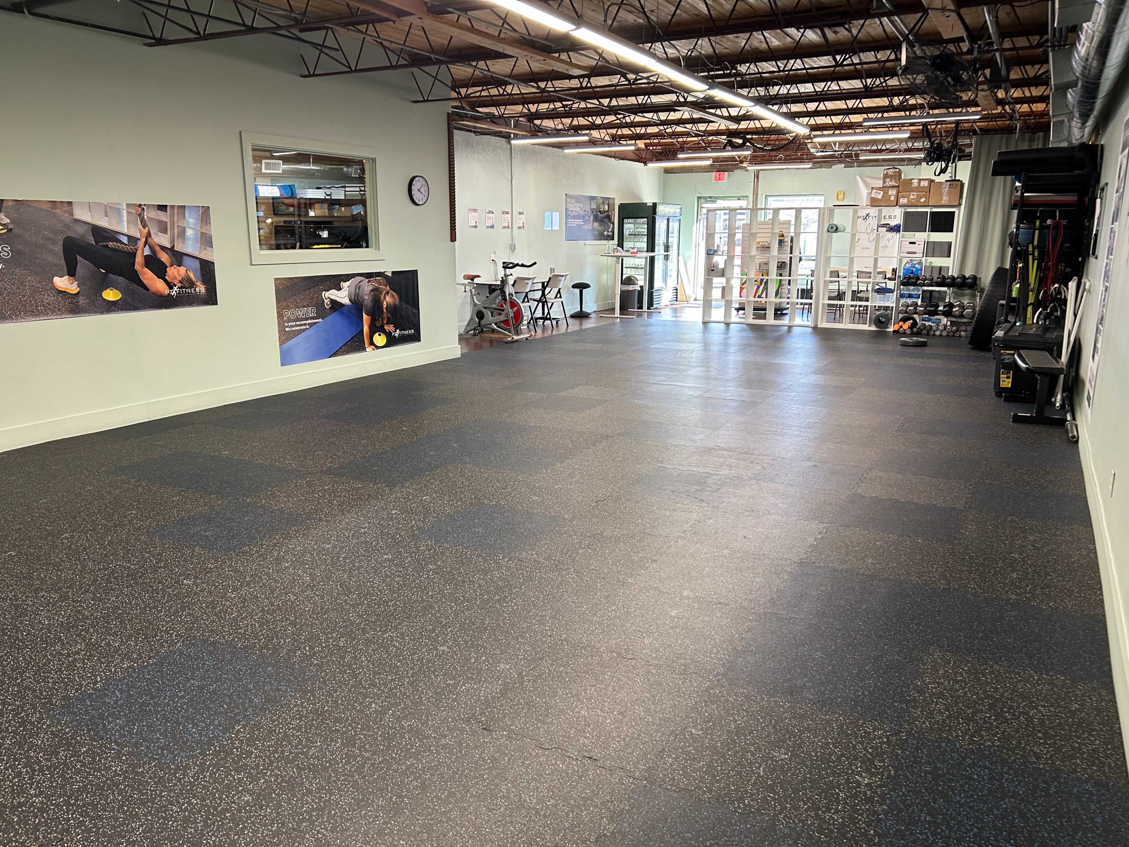 An empty gym or fitness studio with rubber flooring, equipped with exercise equipment and large windows.