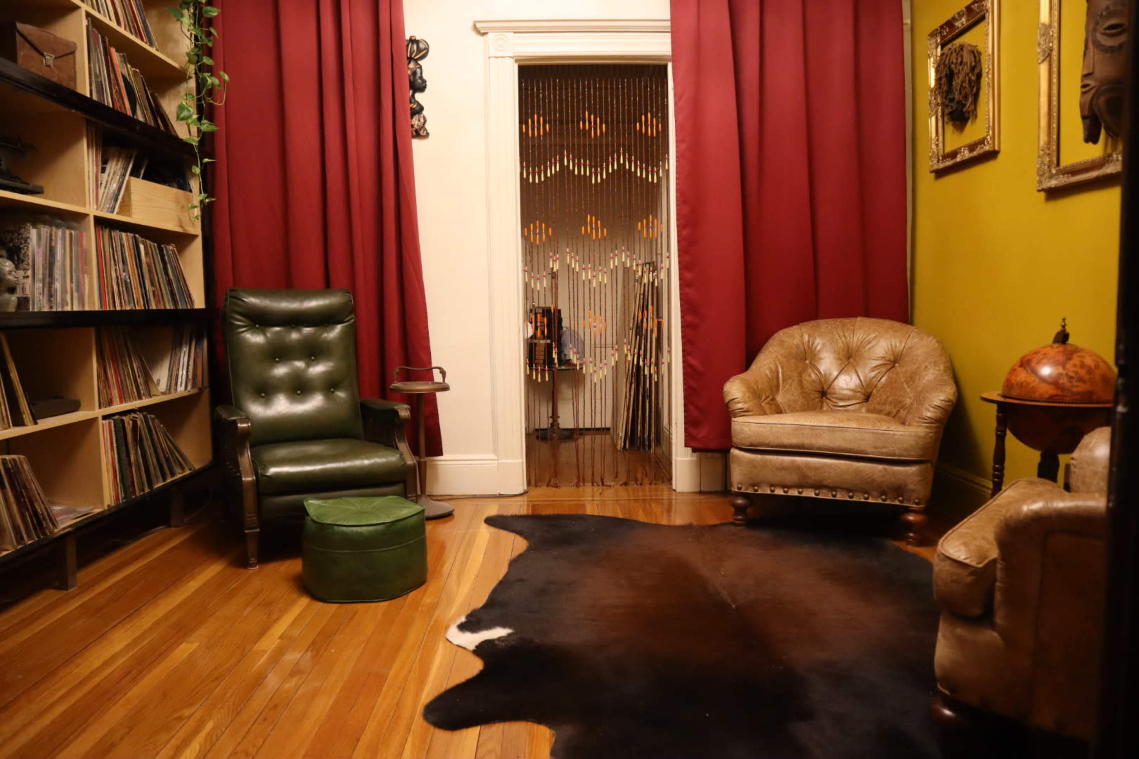 The image shows a cozy room with a record shelf on one side, two armchairs, and a cowhide rug on the wooden floor.