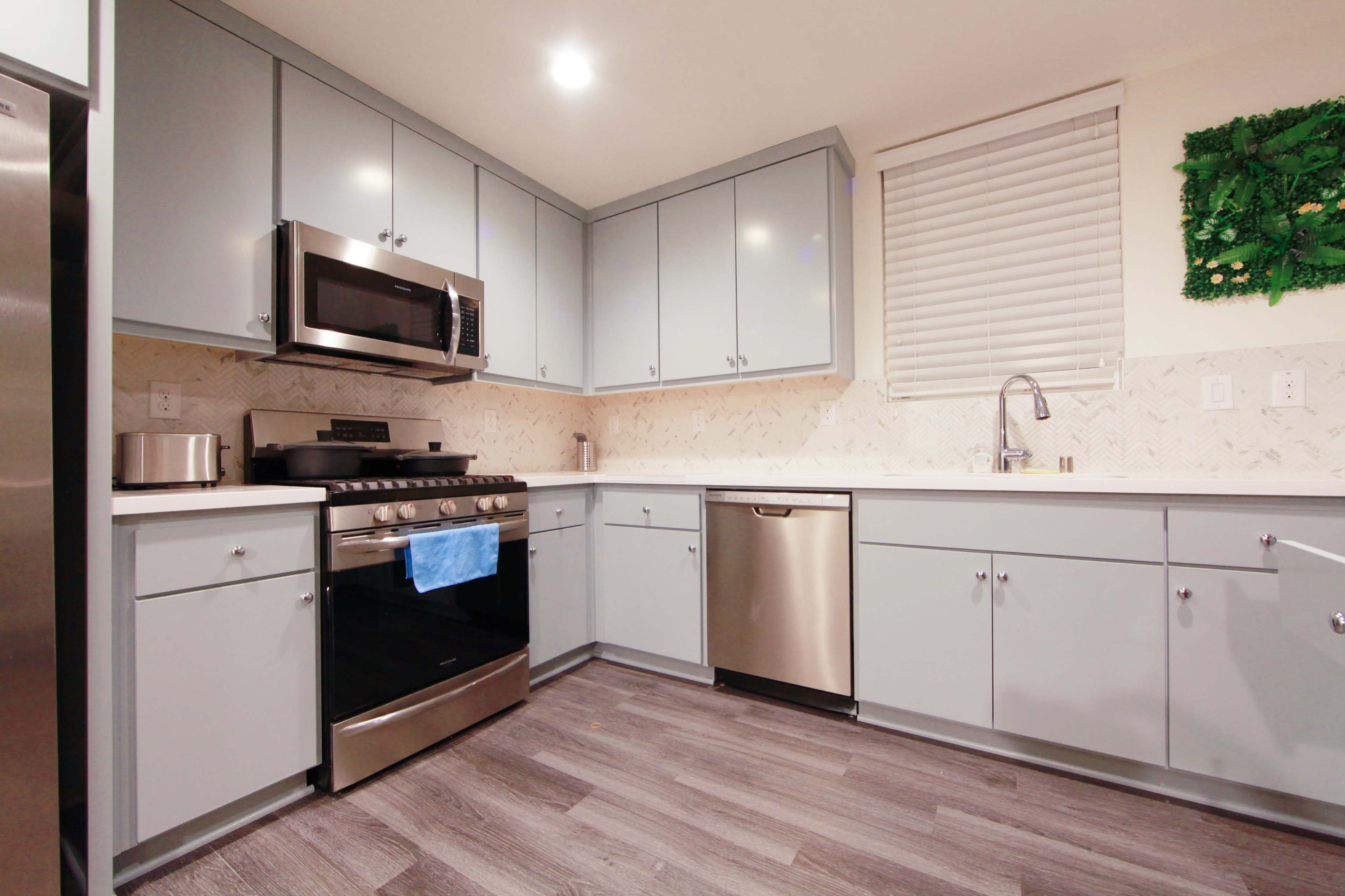 The image shows a modern kitchen with gray cabinets, stainless steel appliances, and a white countertop.
