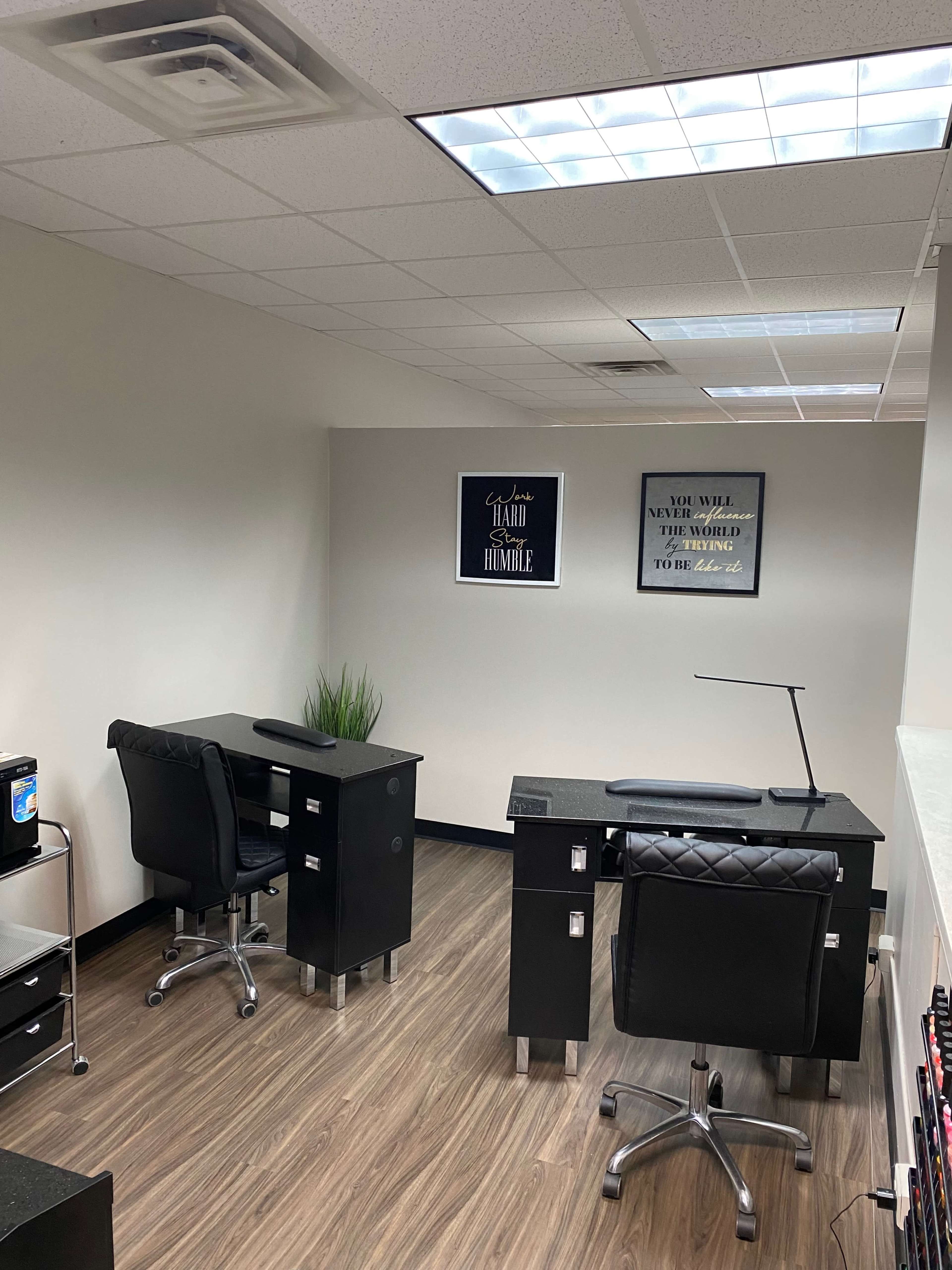 A minimalist office space featuring two black desks with ergonomic chairs and a small plant, illuminated by overhead lighting.