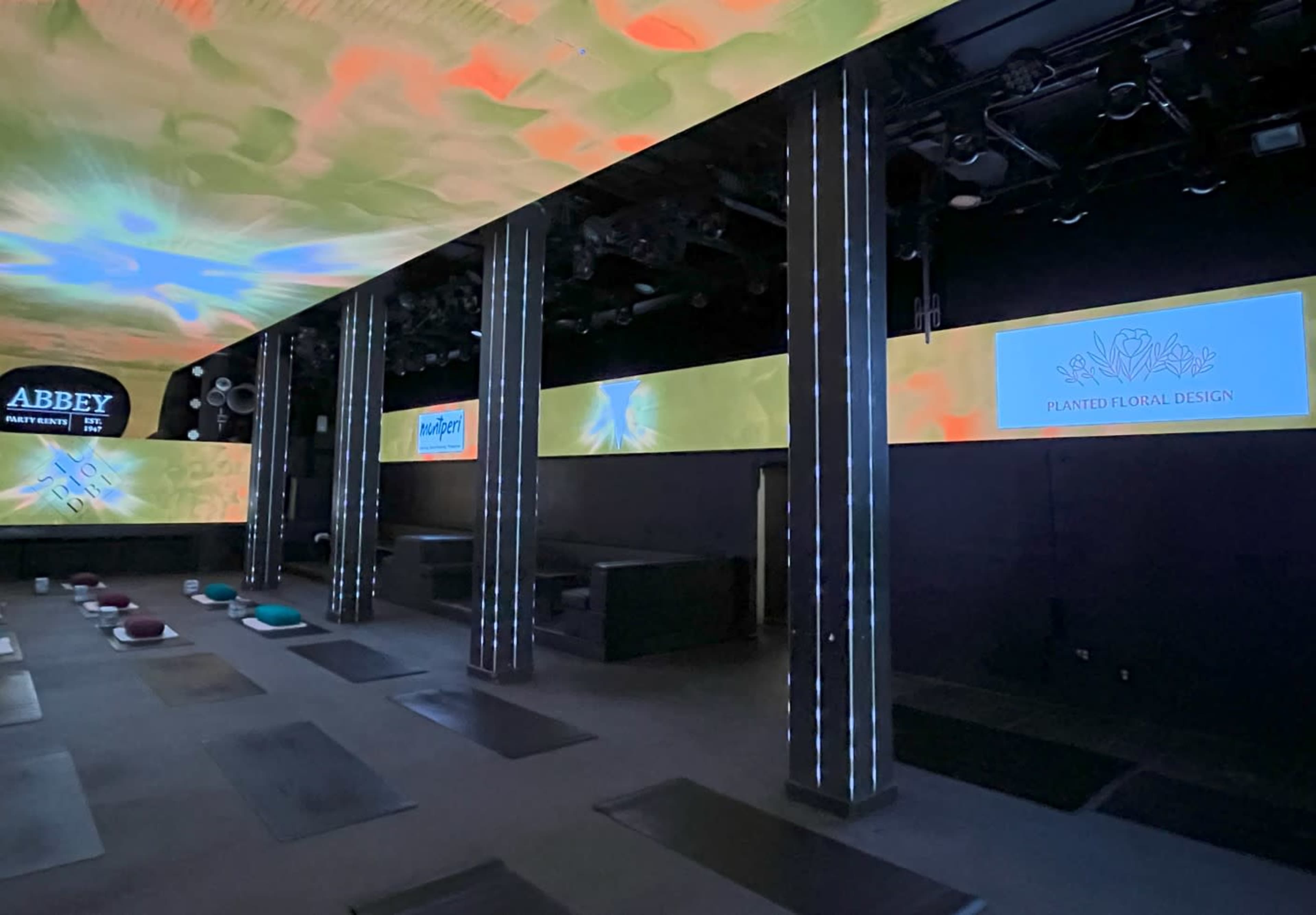 A modern yoga studio with illuminated screens displaying logos and soft color patterns on the ceiling, along with yoga mats arranged on the floor.