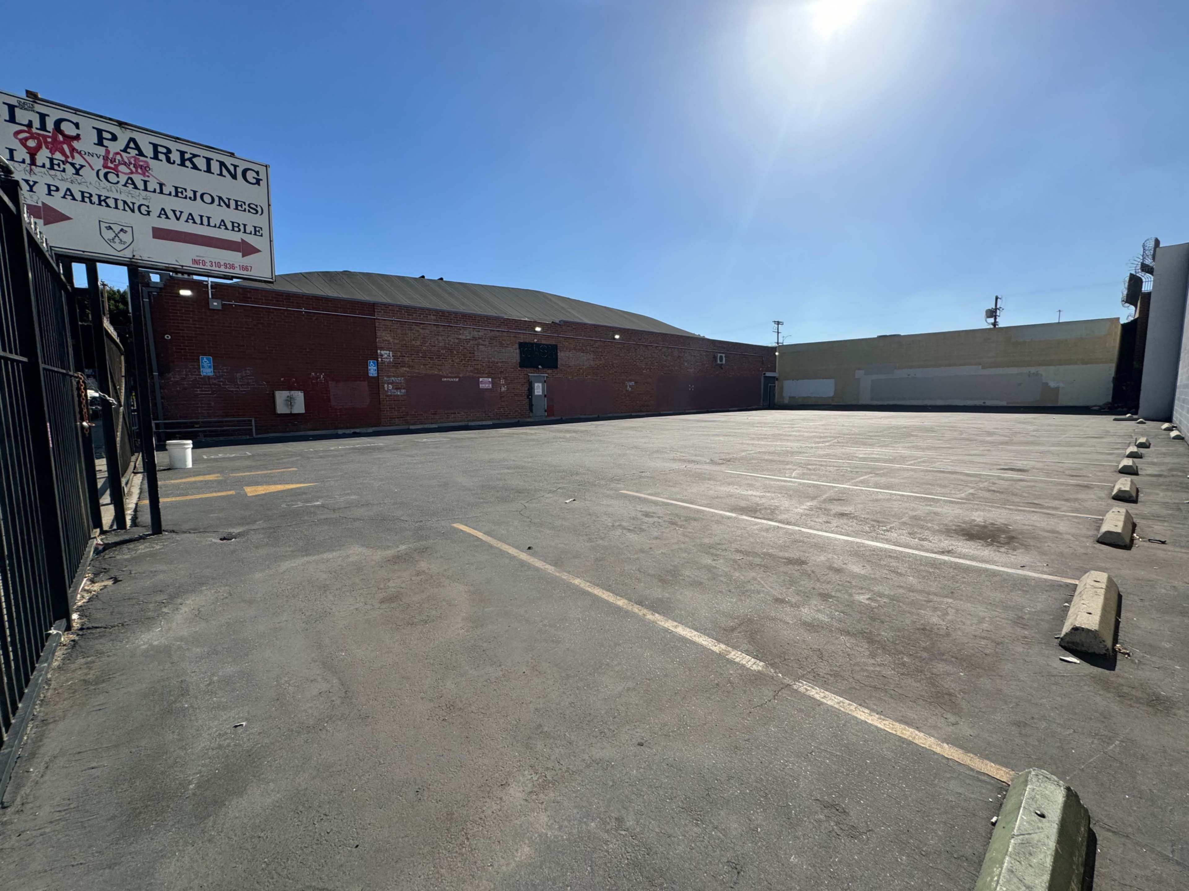 The image shows a large, empty parking lot with marked spaces and a brick building in the background.