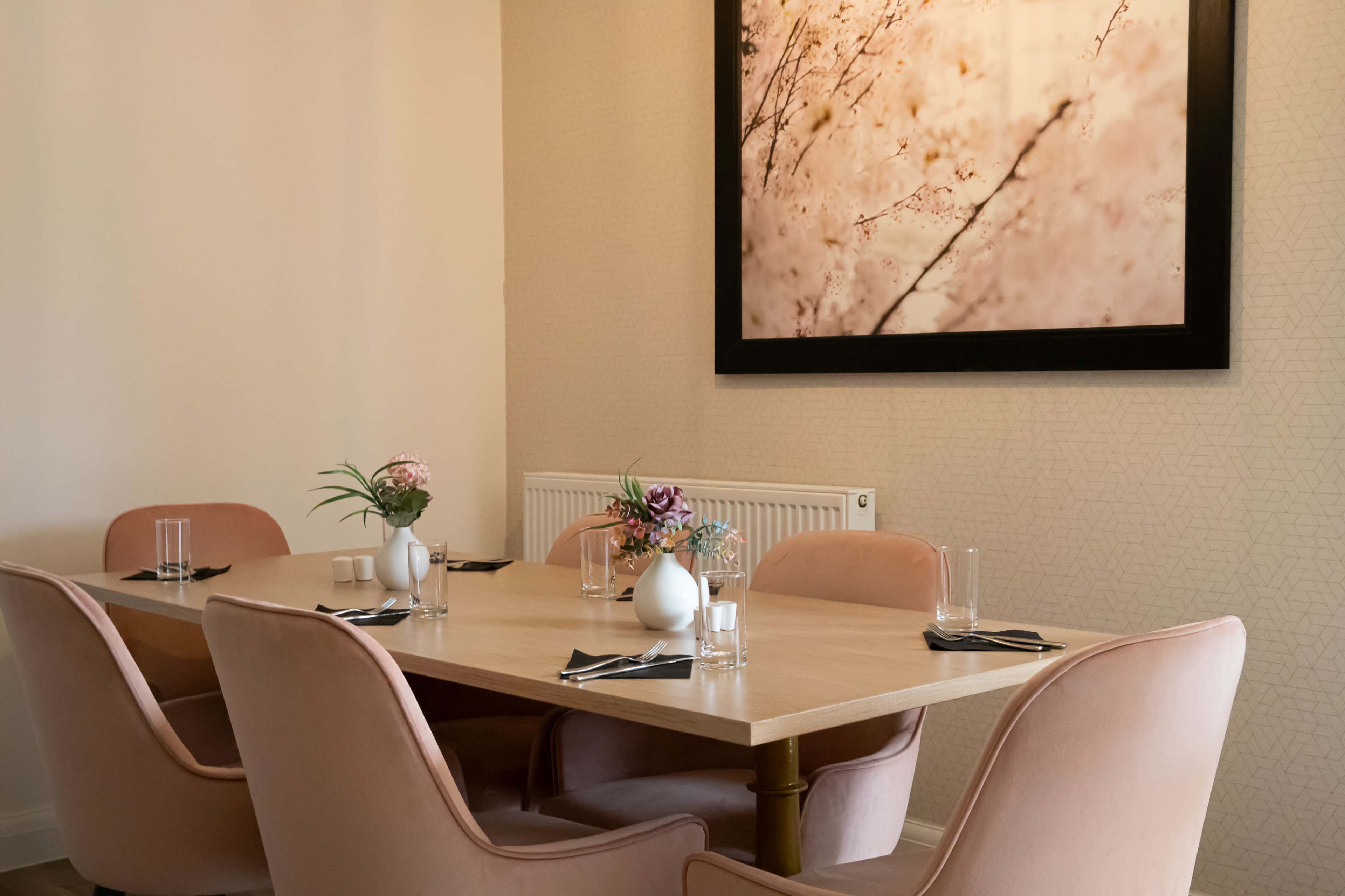 A dining table set for six is positioned in a room with pink upholstered chairs and a large floral photograph on the wall.