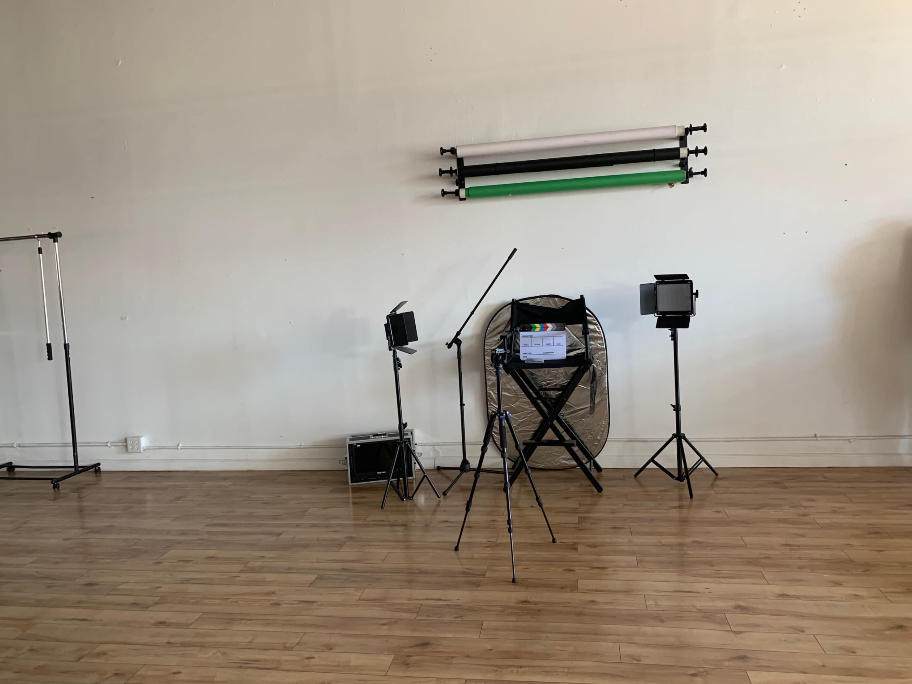 A photography studio with two light stands, a fan, a director's chair, and backdrop support rods mounted on the wall.