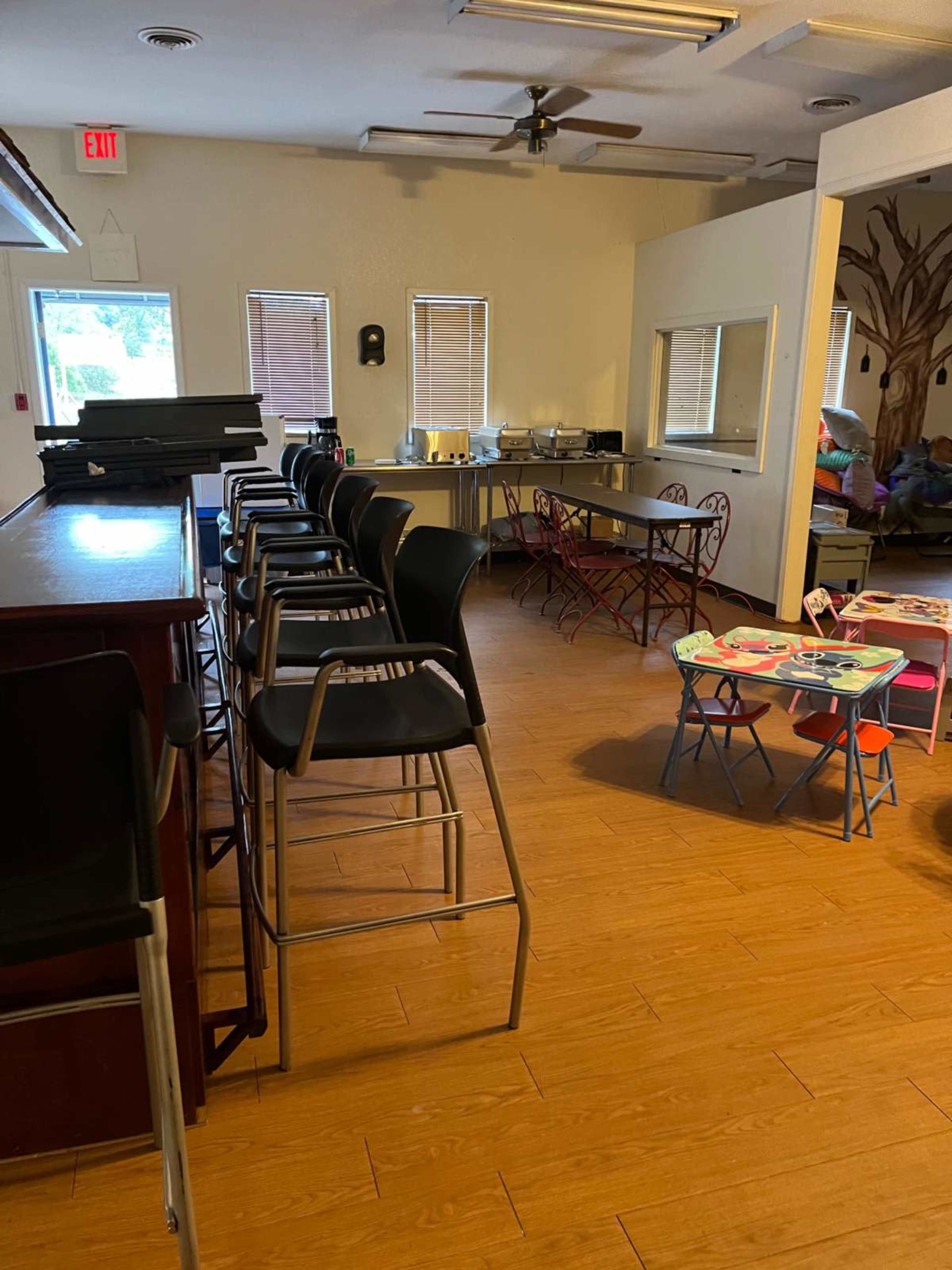 The image shows a room with a bar area featuring high chairs on one side and a table with children’s play equipment on the other side.