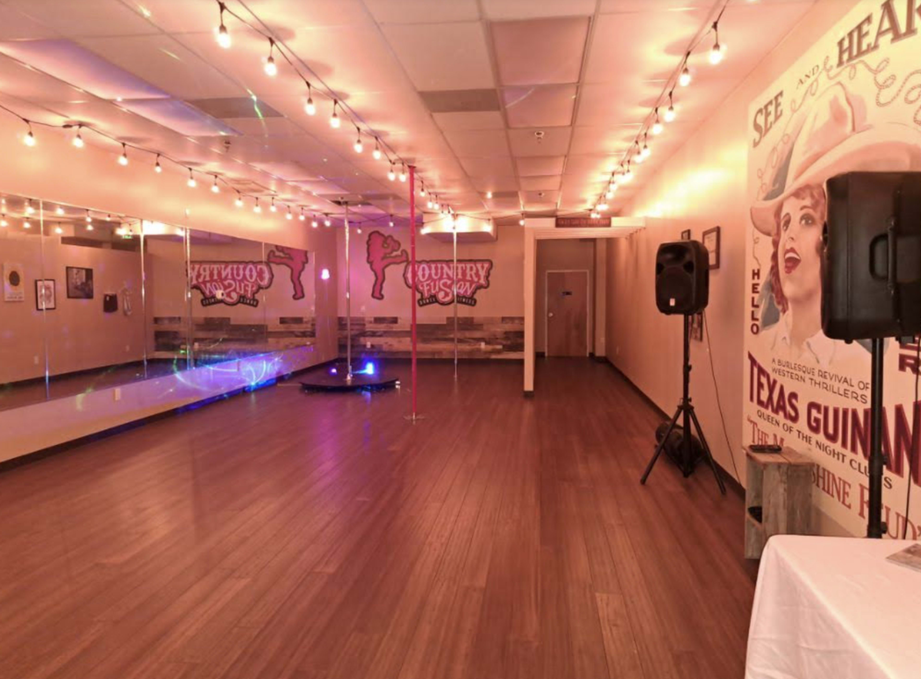 A spacious dance studio with wooden flooring, a mirrored wall, and colorful lighting in a setting decorated with vintage-style posters.