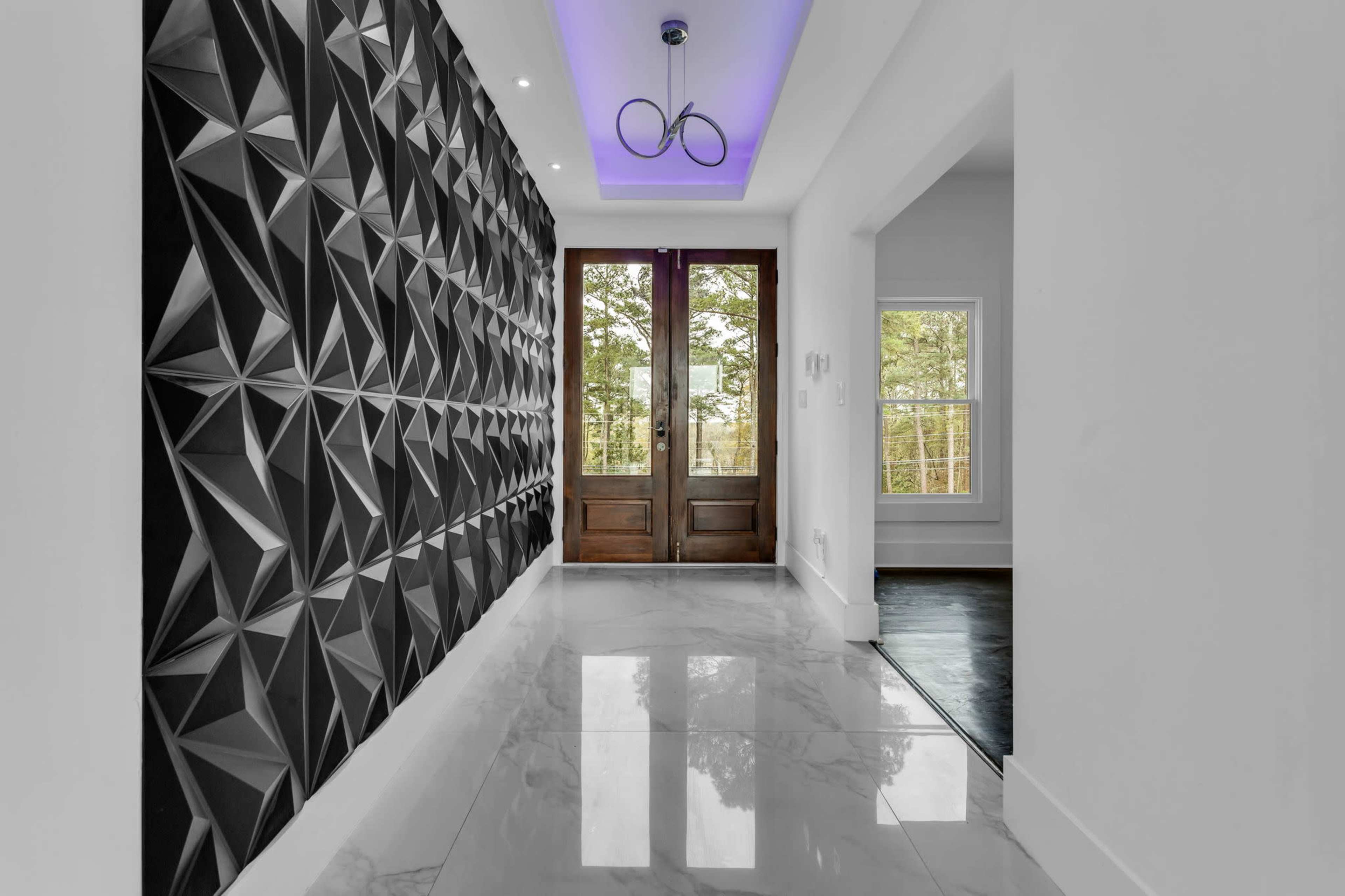 A modern hallway featuring a geometric patterned wall, large double doors, and a glossy tiled floor reflecting ambient light.