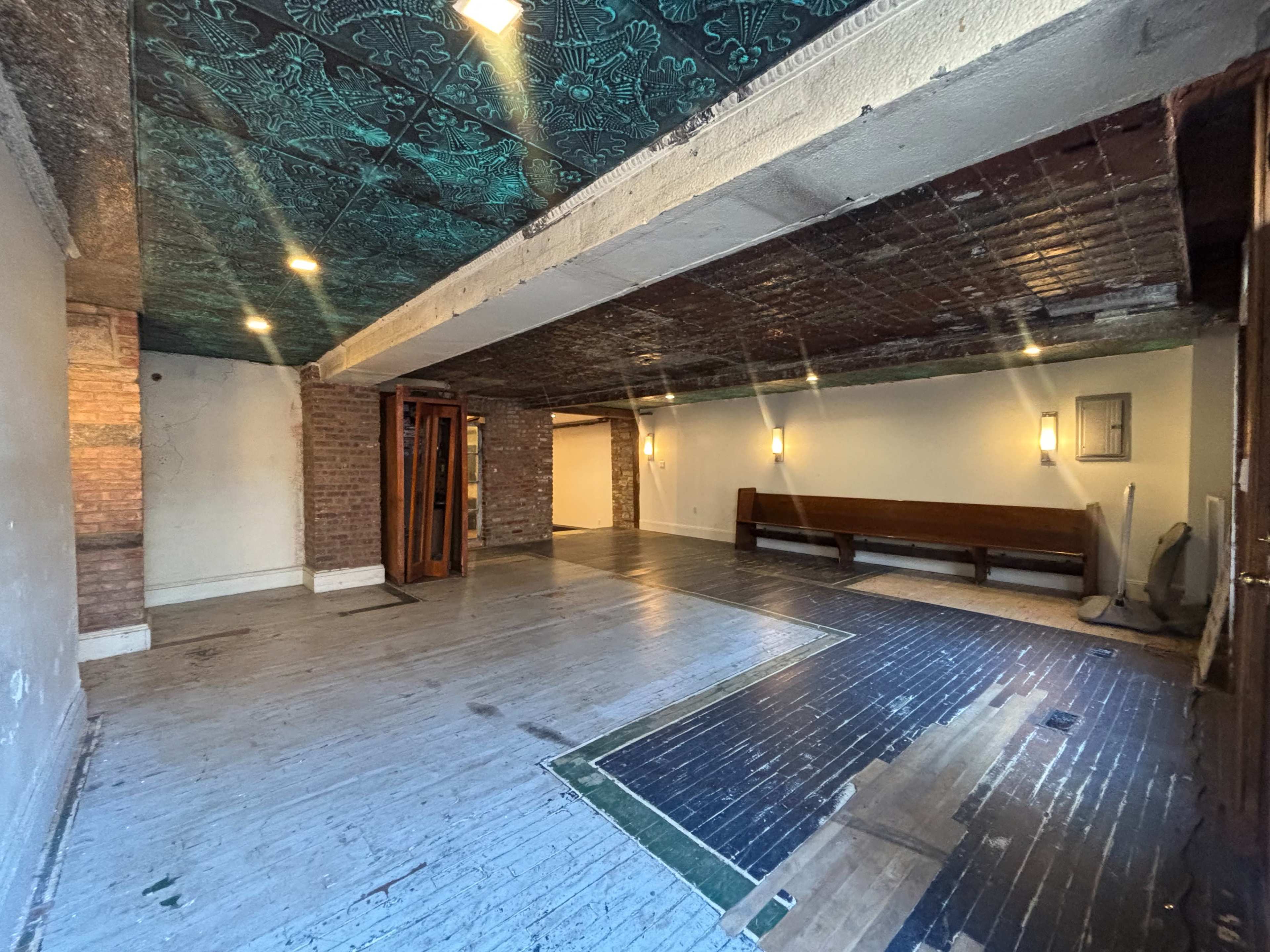 The image shows an empty, partially renovated interior space with varying flooring materials and a decorative ceiling.