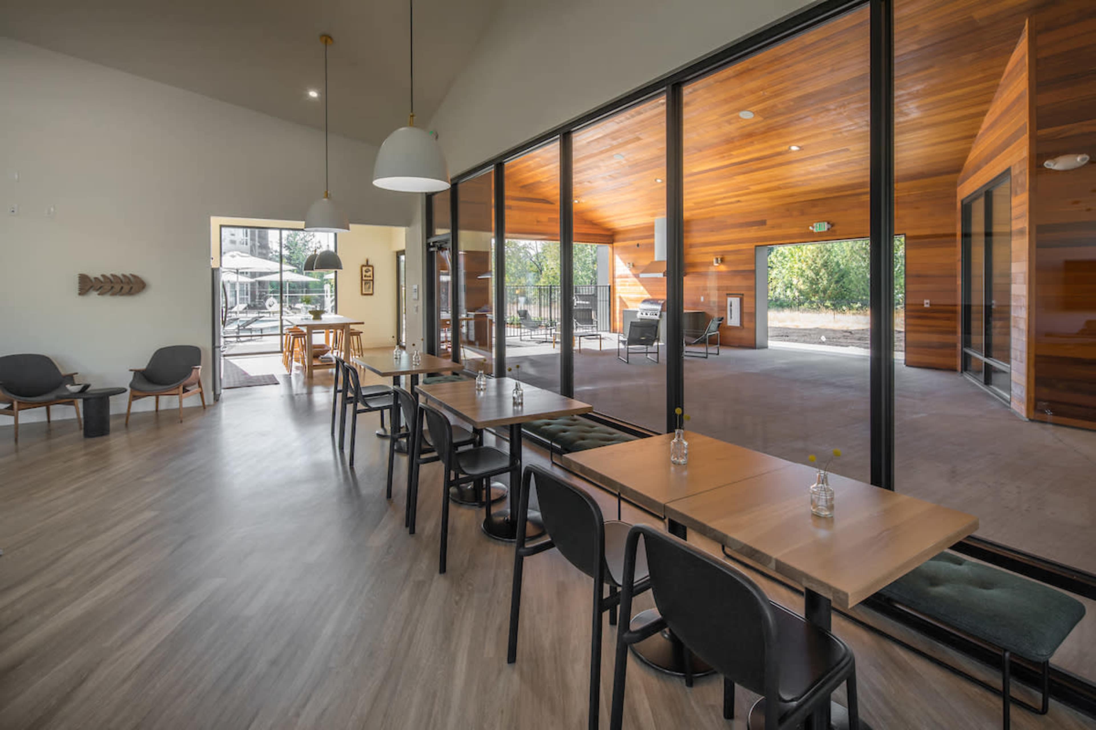 The image shows a modern café interior featuring tables and chairs with large glass sliding doors that open to an outdoor seating area, highlighted by wooden paneling.