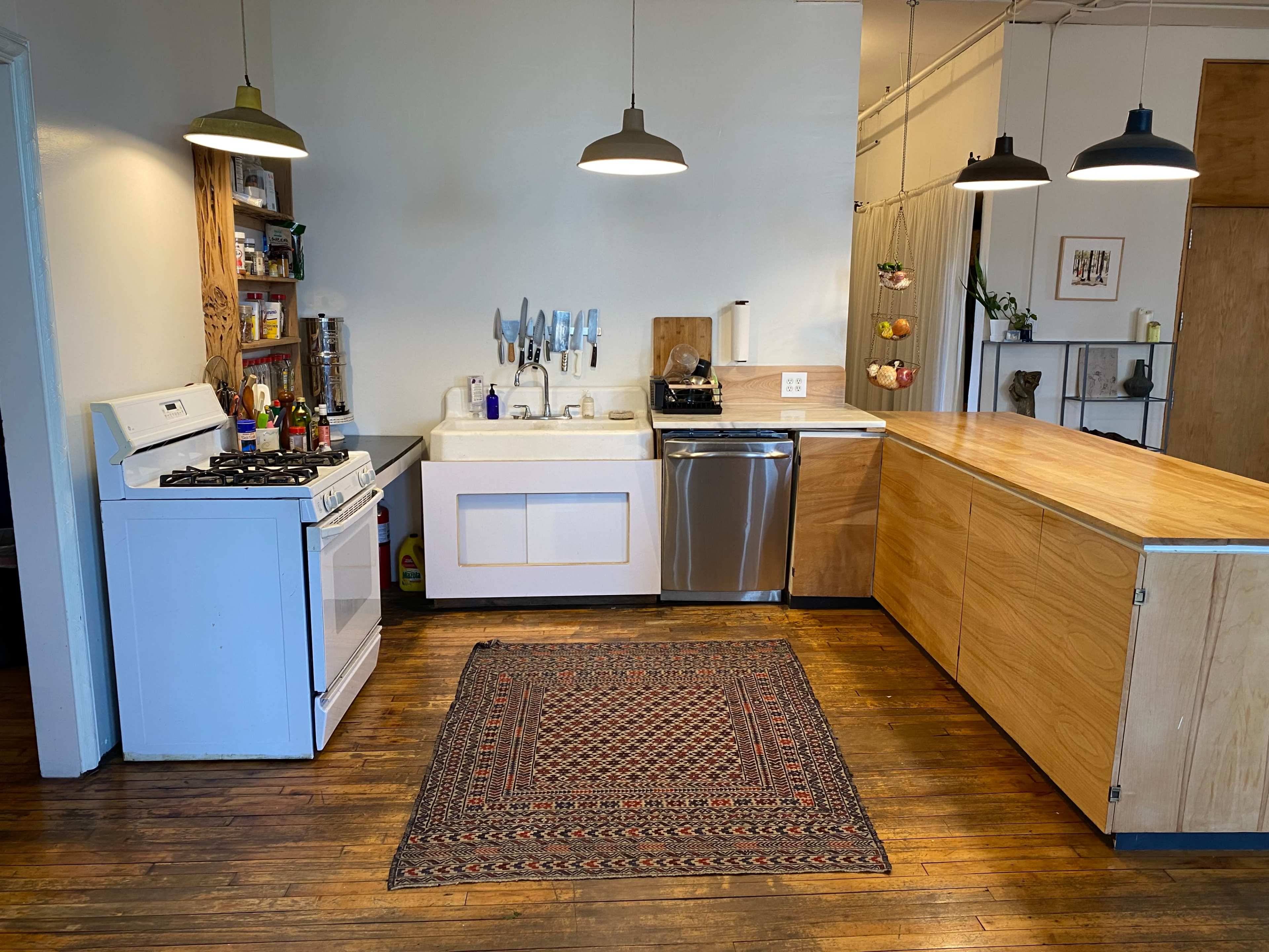 A modern kitchen features a white sink, a gas stove, a stainless steel dishwasher, wooden cabinetry, and a patterned rug on the floor.