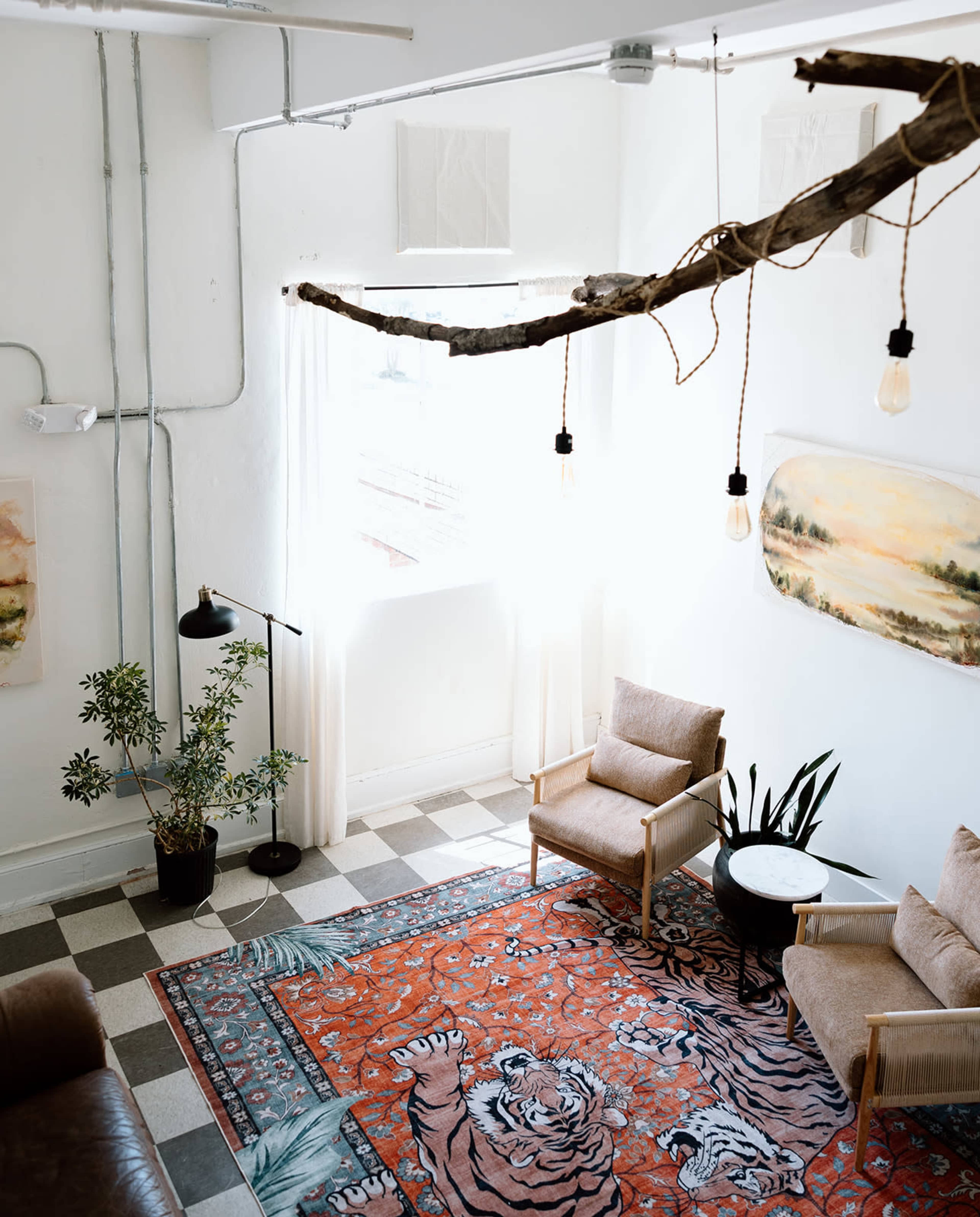 A cozy living space features two armchairs, a tiger-patterned rug, a plant, and large windows allowing natural light to illuminate the room.