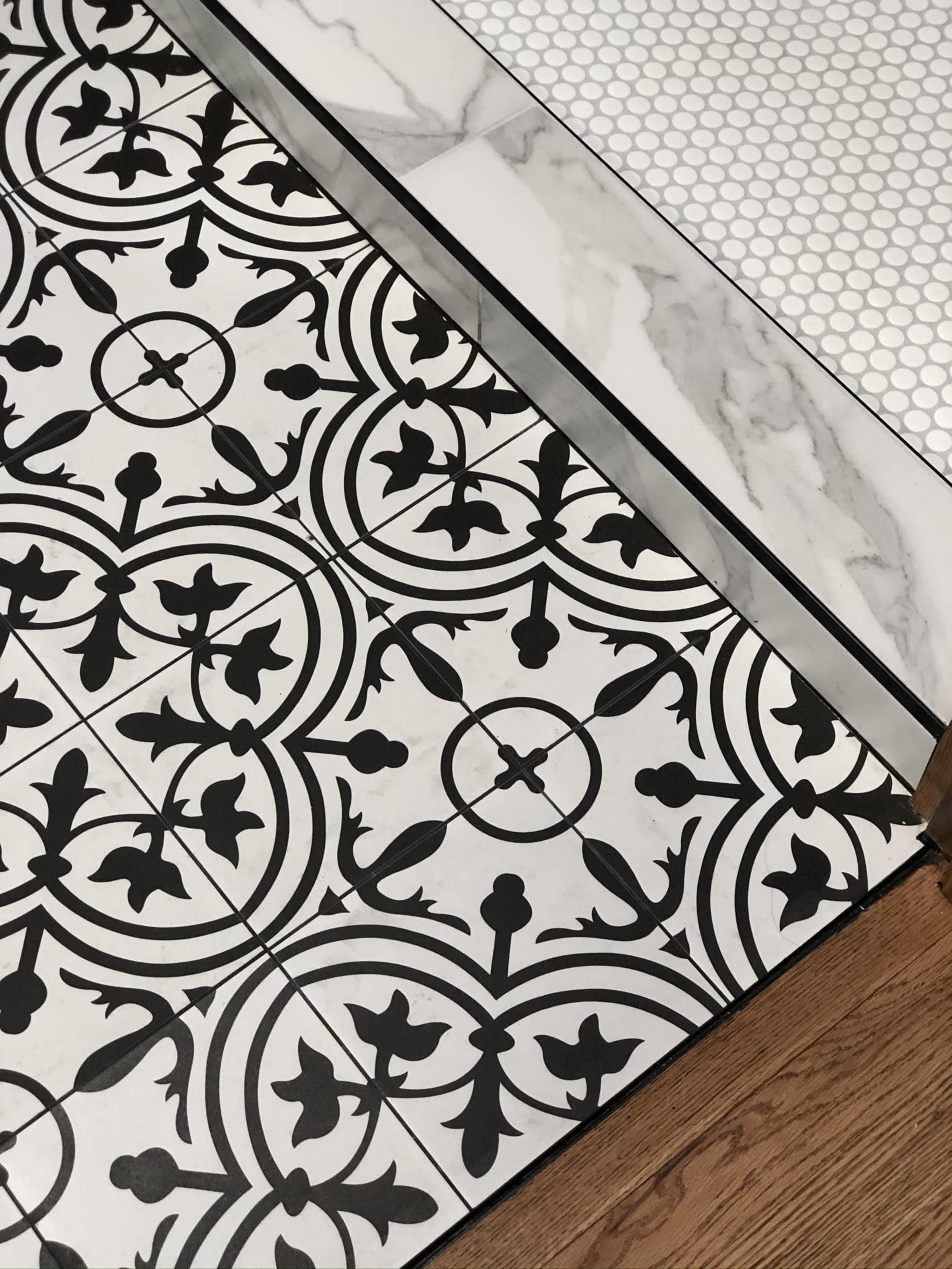 Two contrasting floor tile designs: a black and white patterned tile adjacent to a white hexagonal tile, with a wooden edge visible at the lower corner.