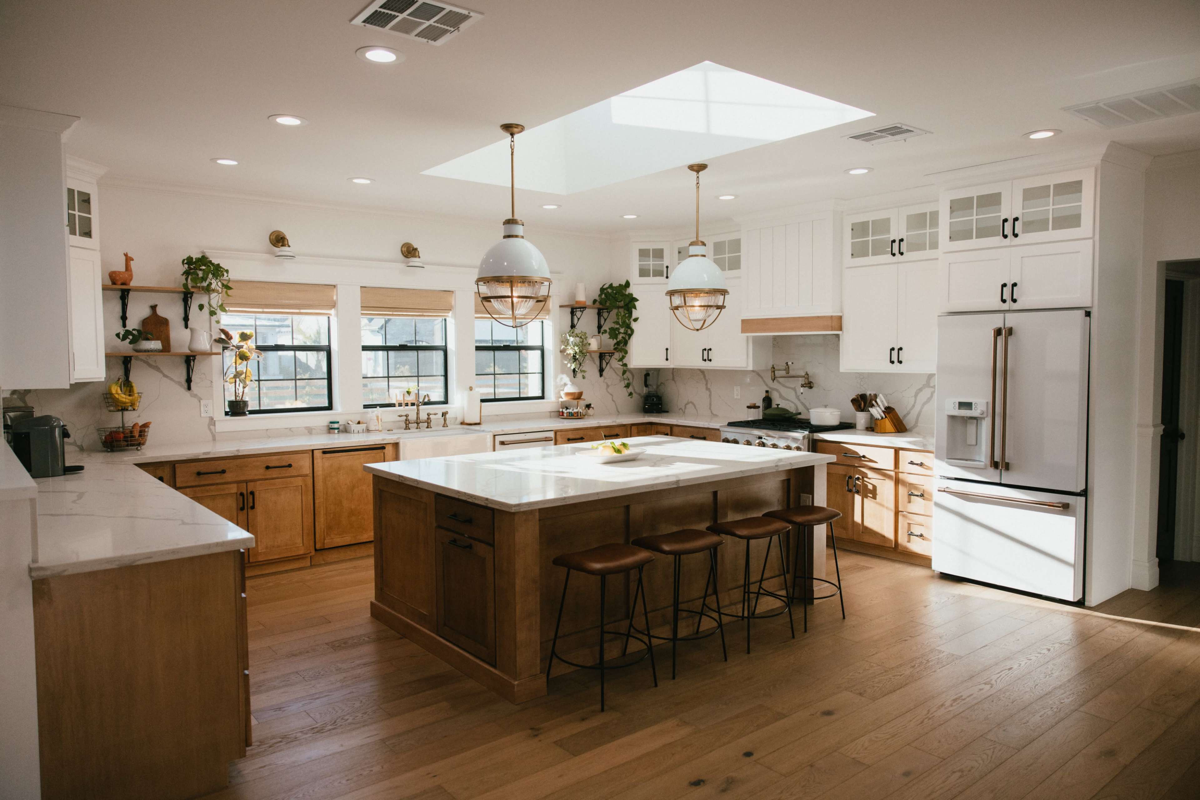 A modern kitchen features a central island with three stools, white cabinetry, wooden accents, and a skylight that illuminates the space.