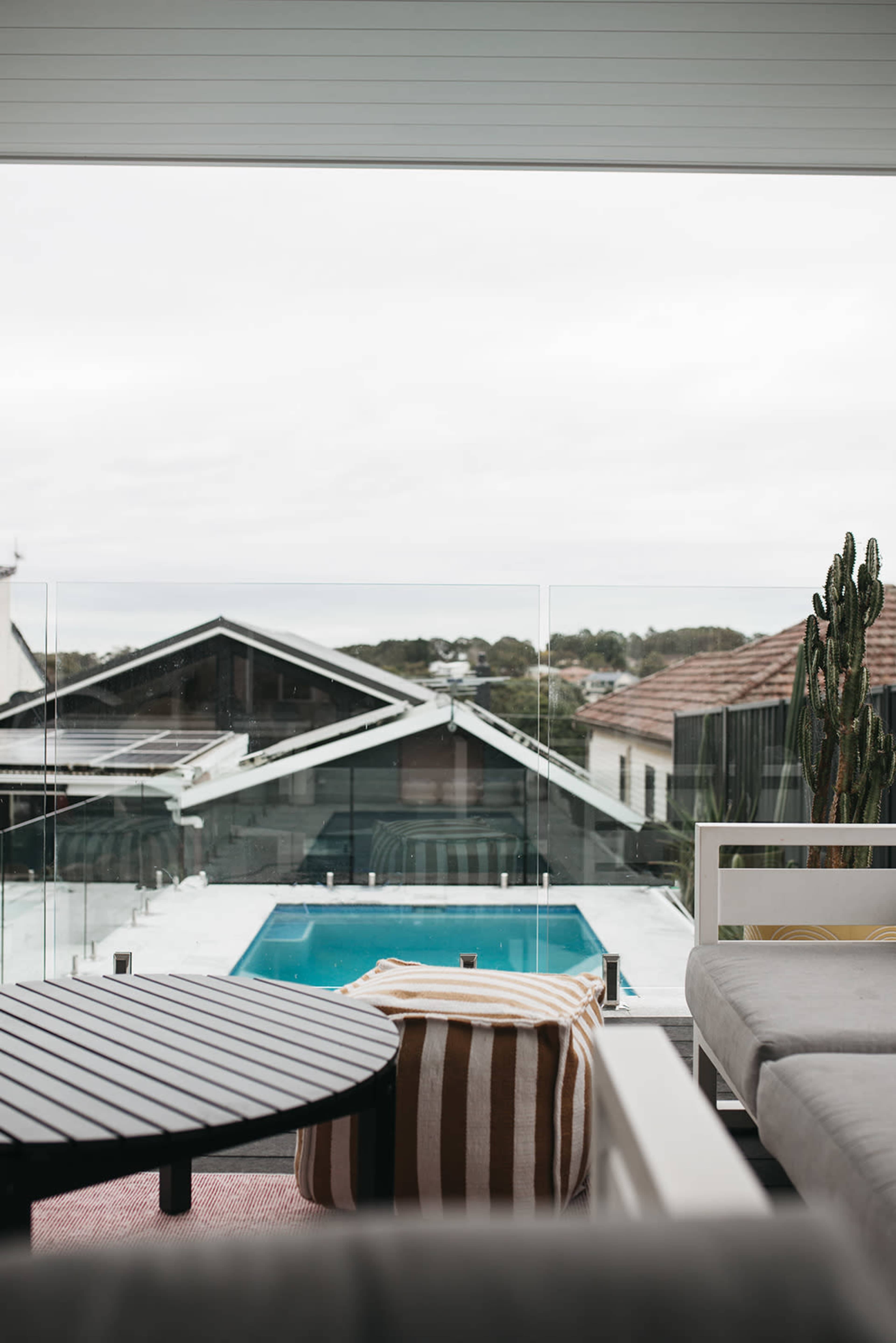A modern outdoor patio featuring a table and seating area, overlooking a swimming pool surrounded by buildings and greenery.