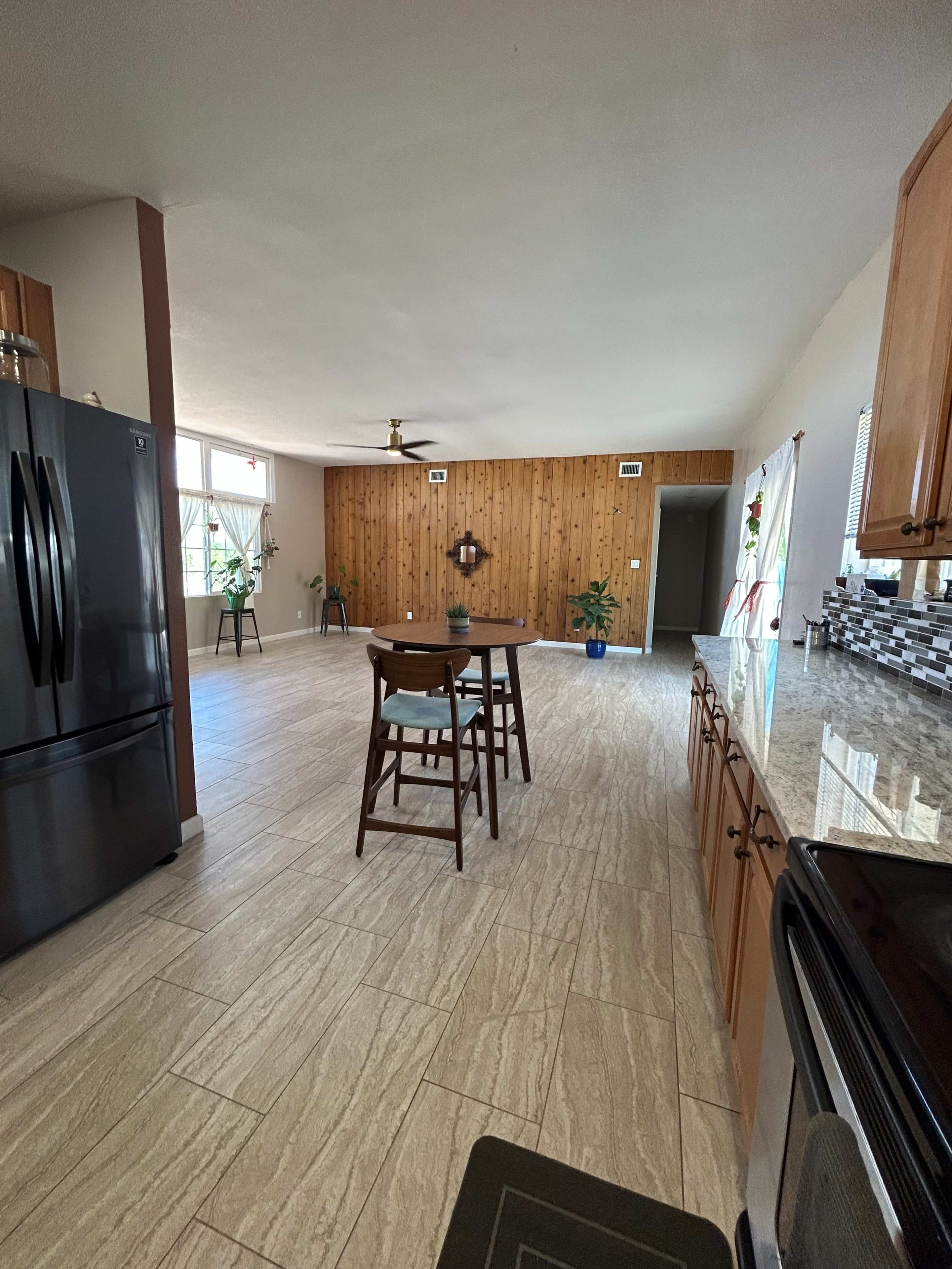 A spacious kitchen features wooden paneling, granite countertops, a black refrigerator, and a central table with chairs.