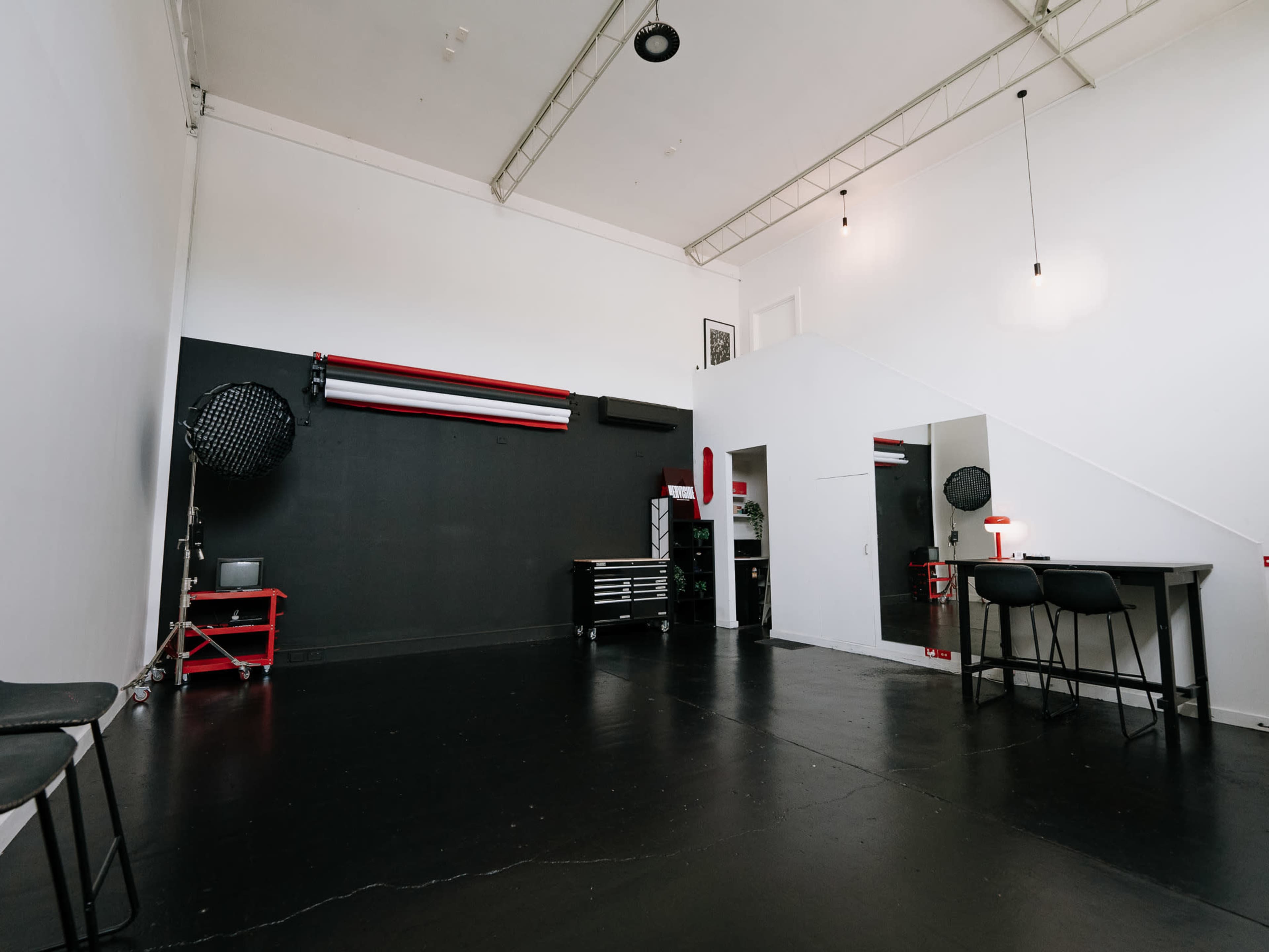The image shows a spacious, minimalist studio with a black wall, a worktable, a mirror, and a red tool cart.