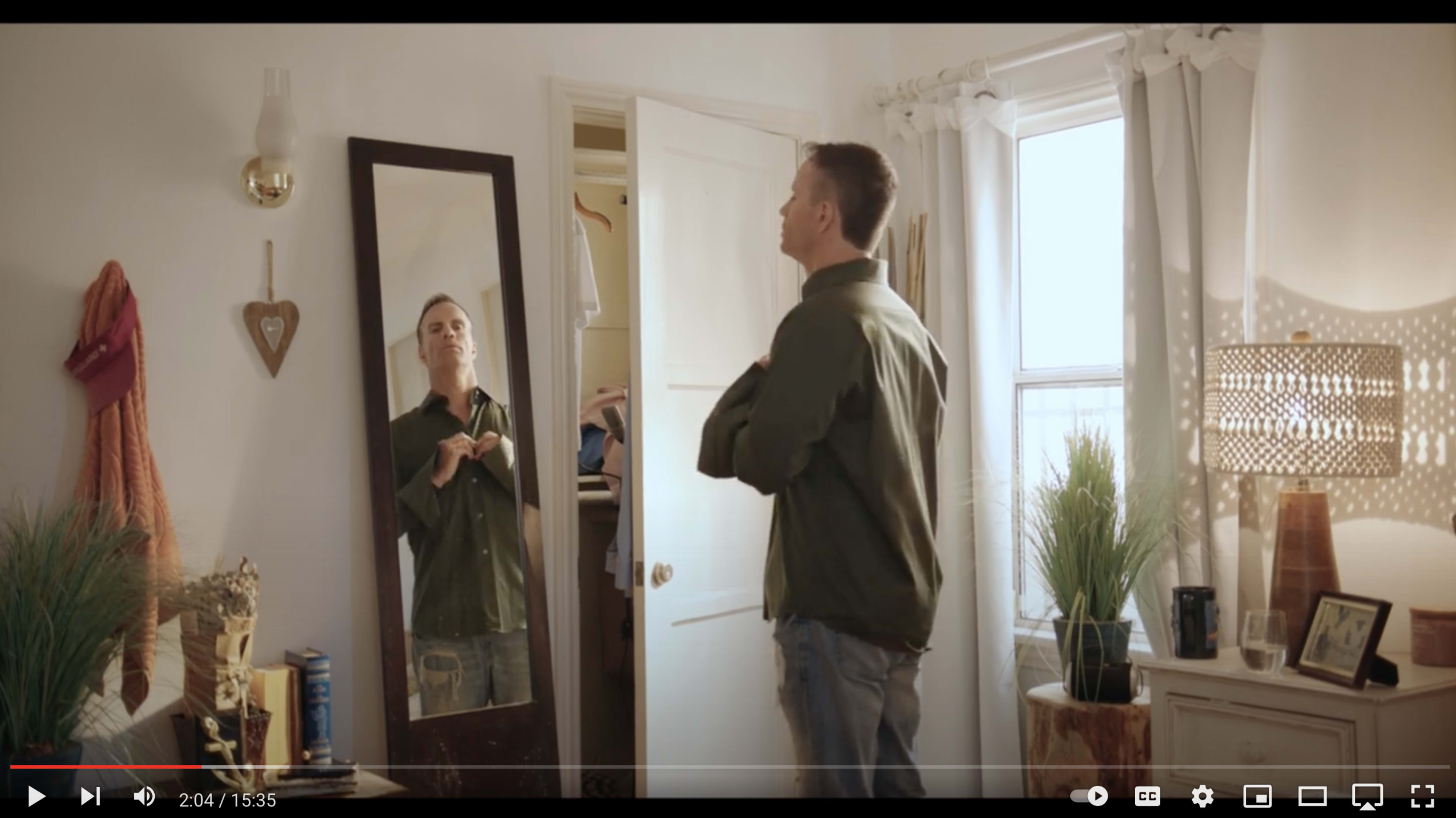 A man stands in front of a mirror adjusting his jacket in a well-lit room.