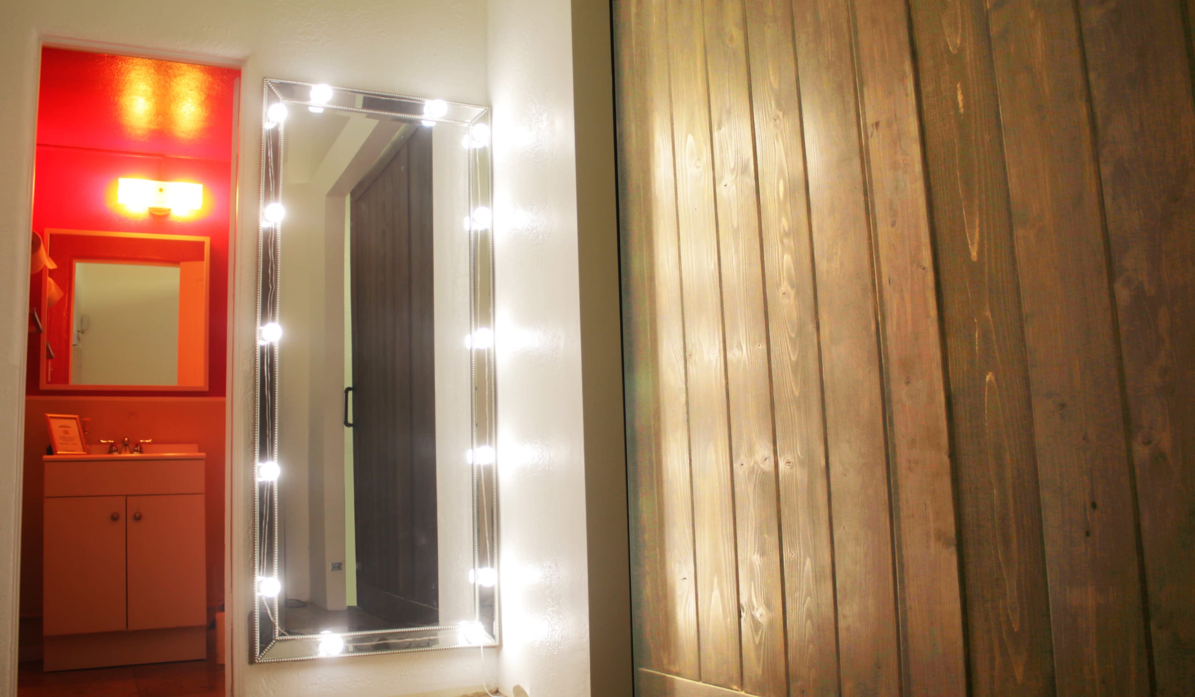 A brightly lit mirror is mounted on a wall next to a wooden panel.