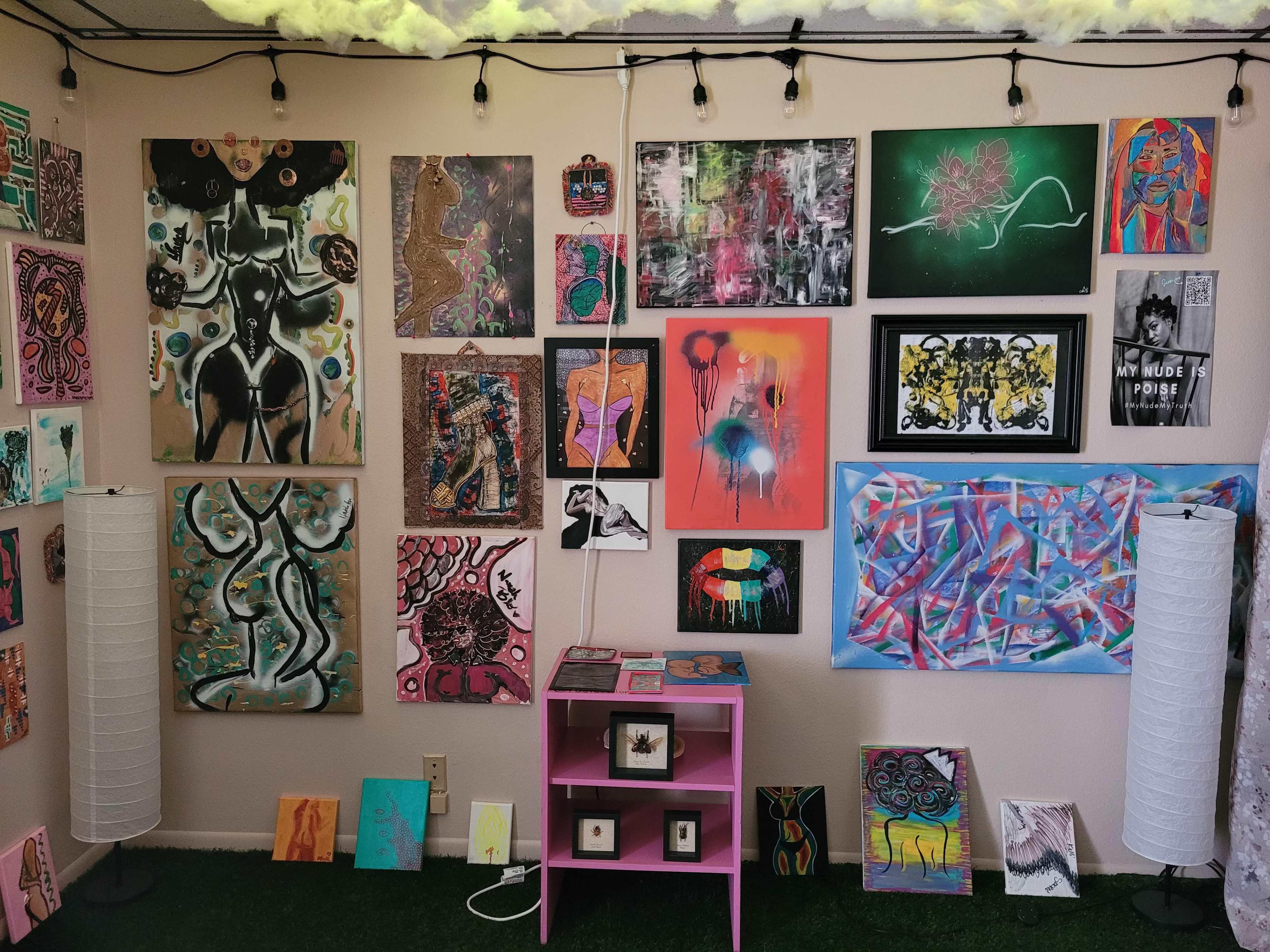 A room with a collection of various artworks displayed on the walls, accompanied by a pink table and decorative lamps.