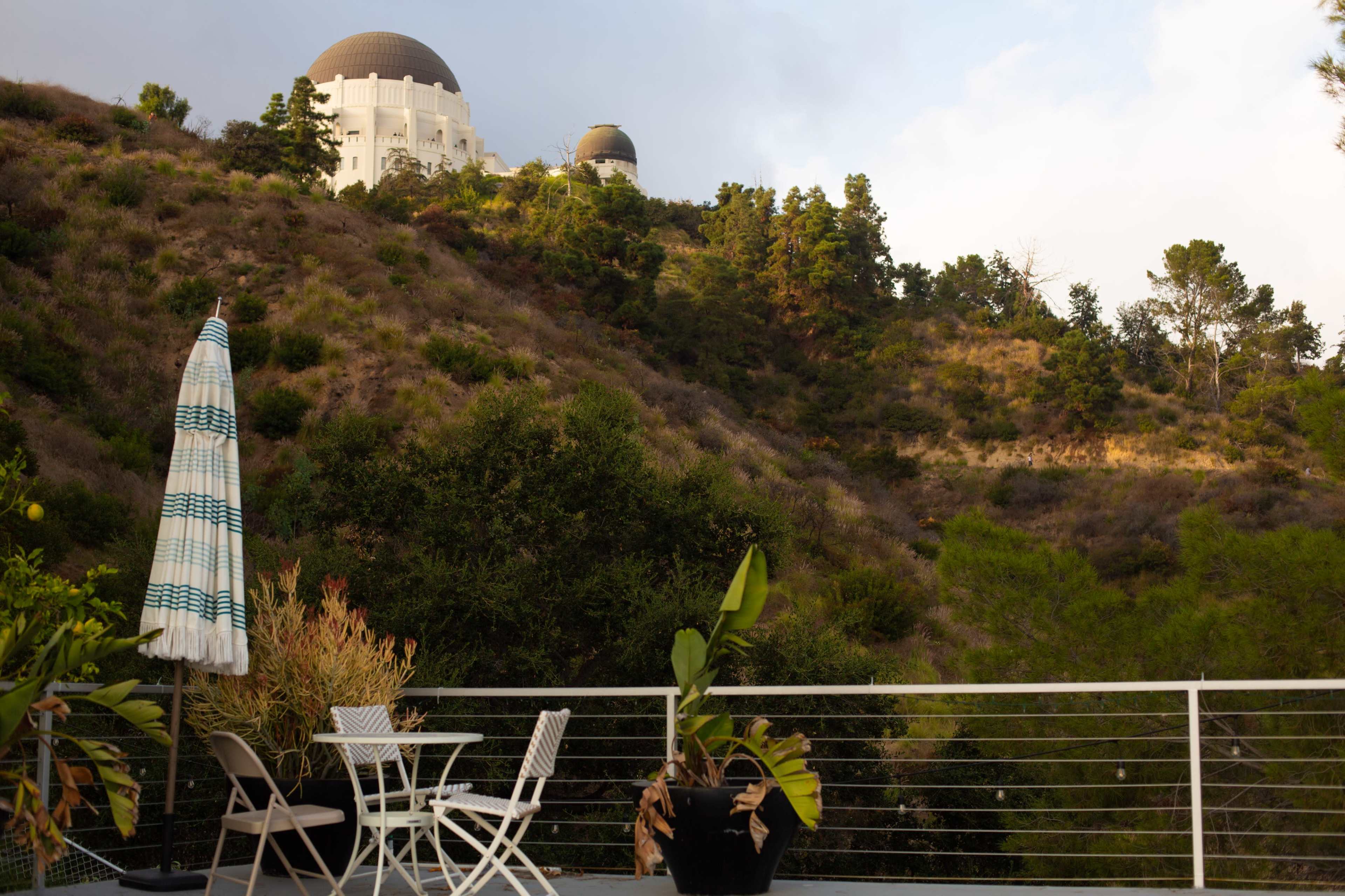 The image shows a terrace with a small table and chairs, overlooking a hillside with a large observatory dome perched on top.