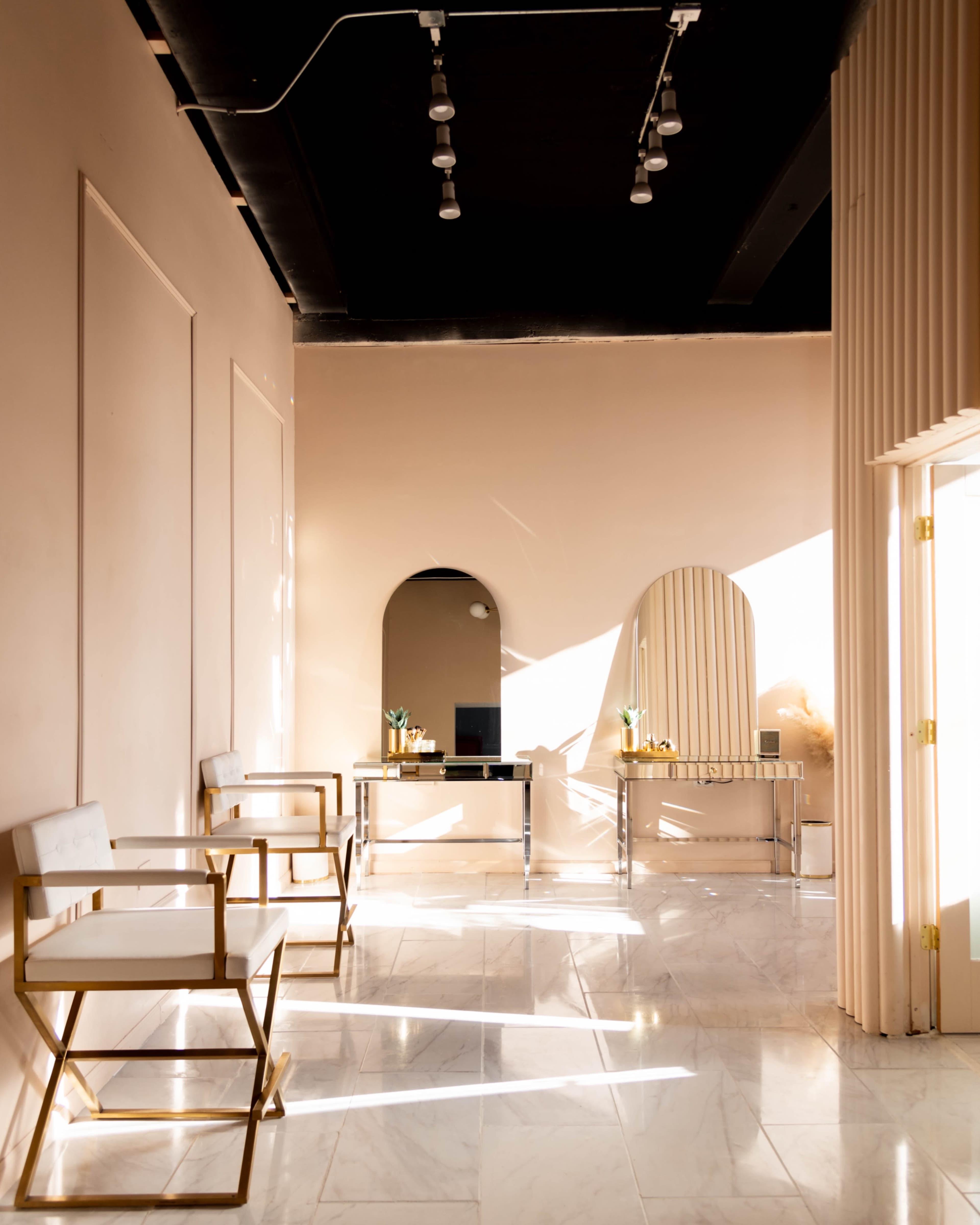 A modern interior space with two chairs, a mirror, and two tables, all illuminated by natural light filtering through the windows.
