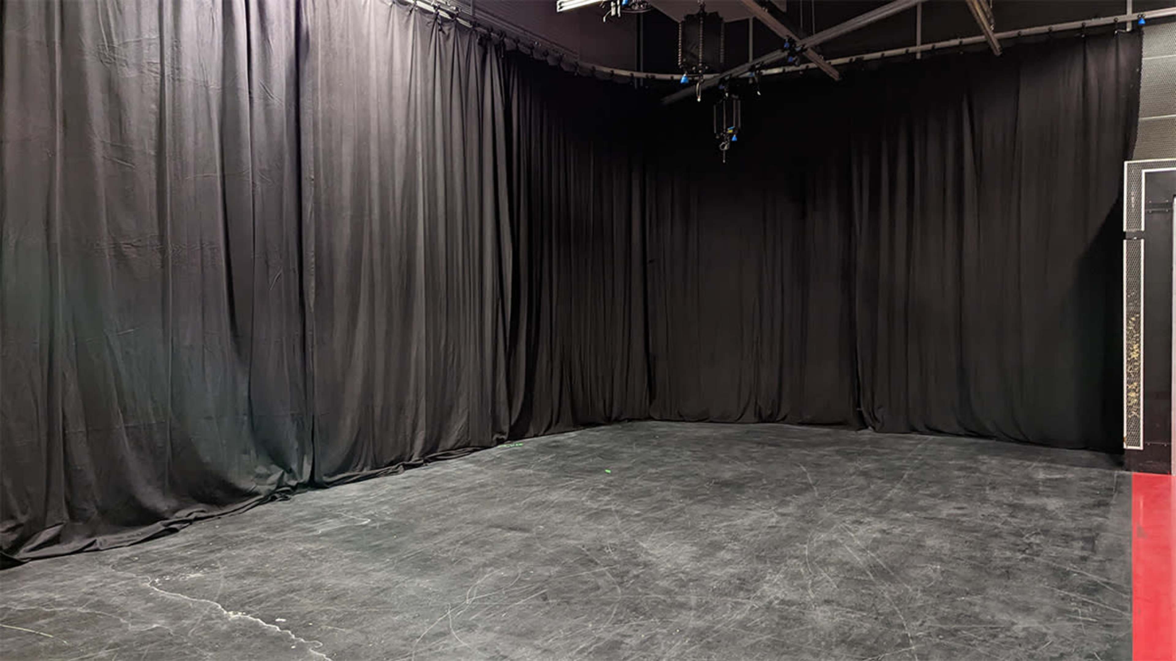 A spacious studio with black curtains lining the walls and a polished concrete floor.