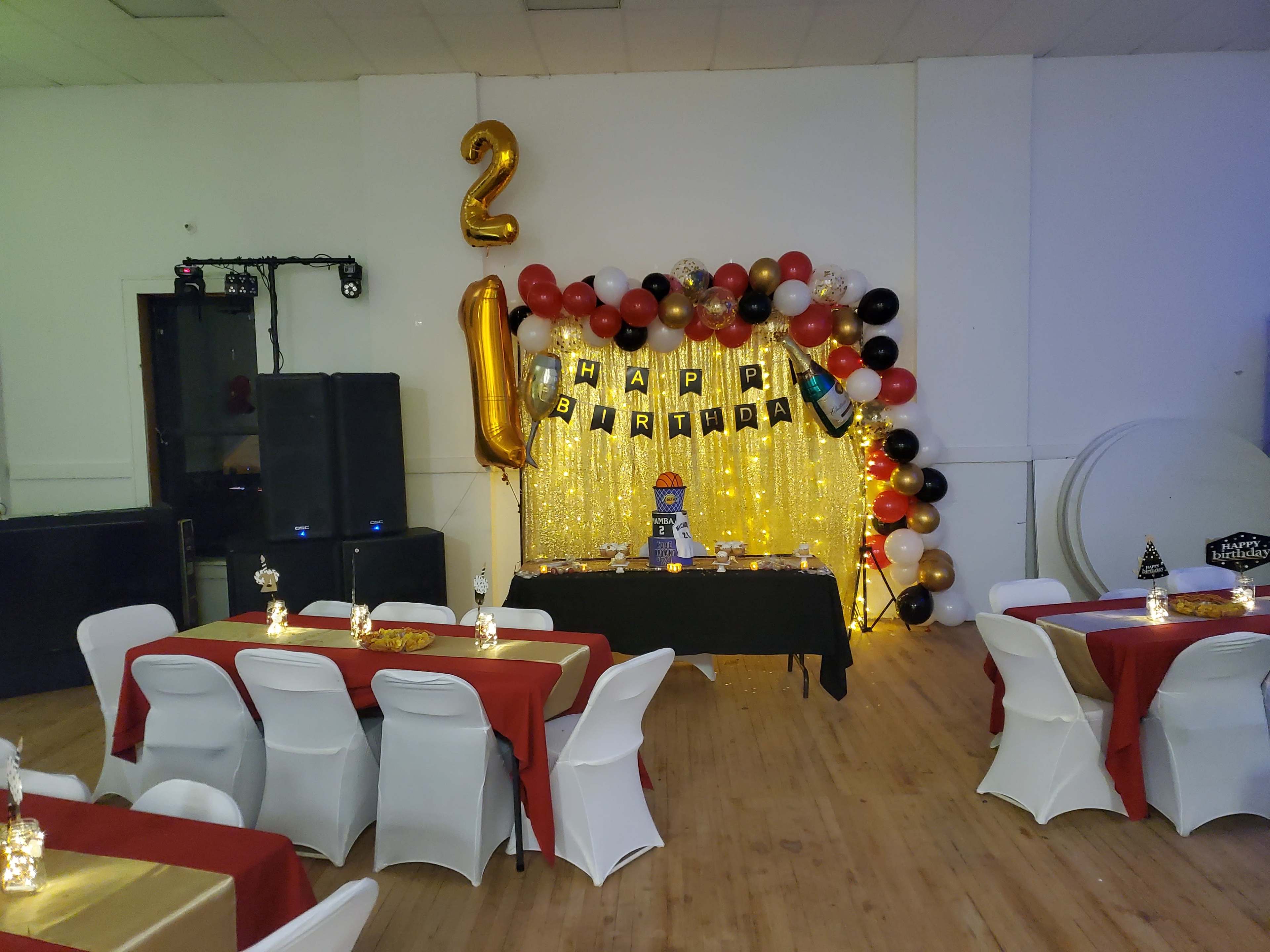 The scene features a decorated party area with a "Happy Birthday" banner, a table set with a blue cake, and tables adorned with red tablecloths and white chairs.