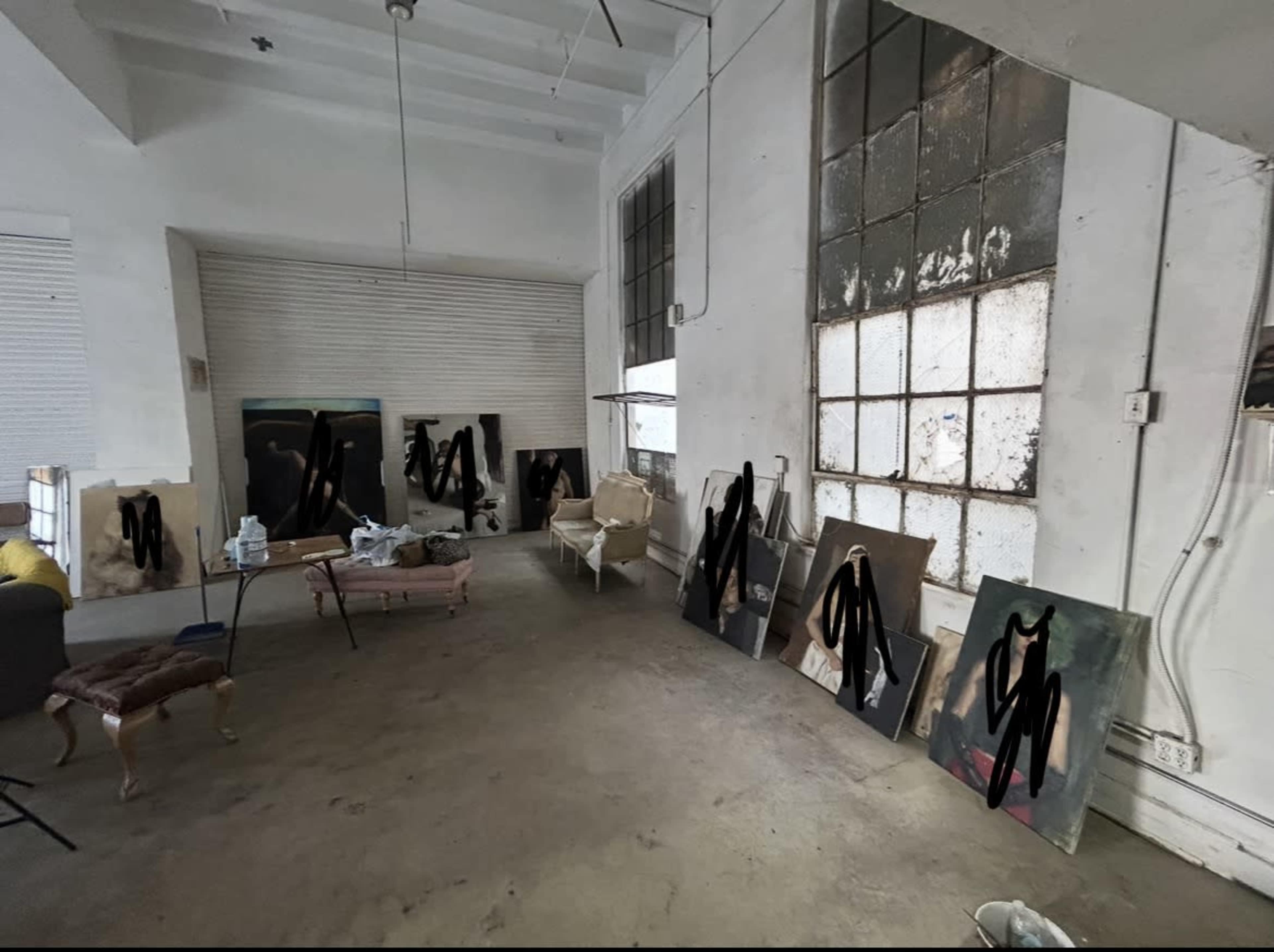 The image shows an empty art studio with several canvases leaning against the walls and remnants of painting materials scattered on the floor.