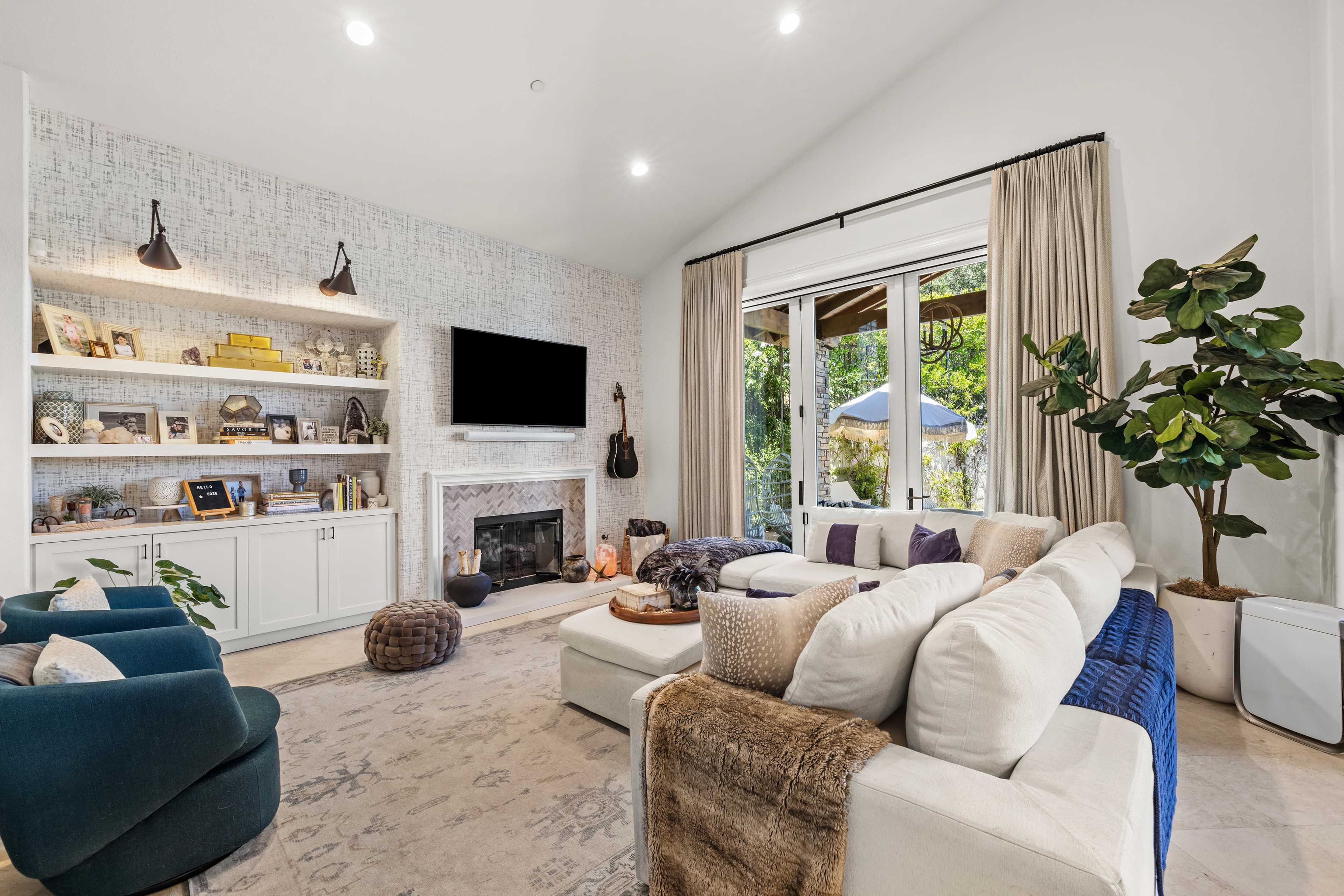 The living room features a white sofa, blue accent chairs, a built-in shelf with decorative items, and large windows with natural light.