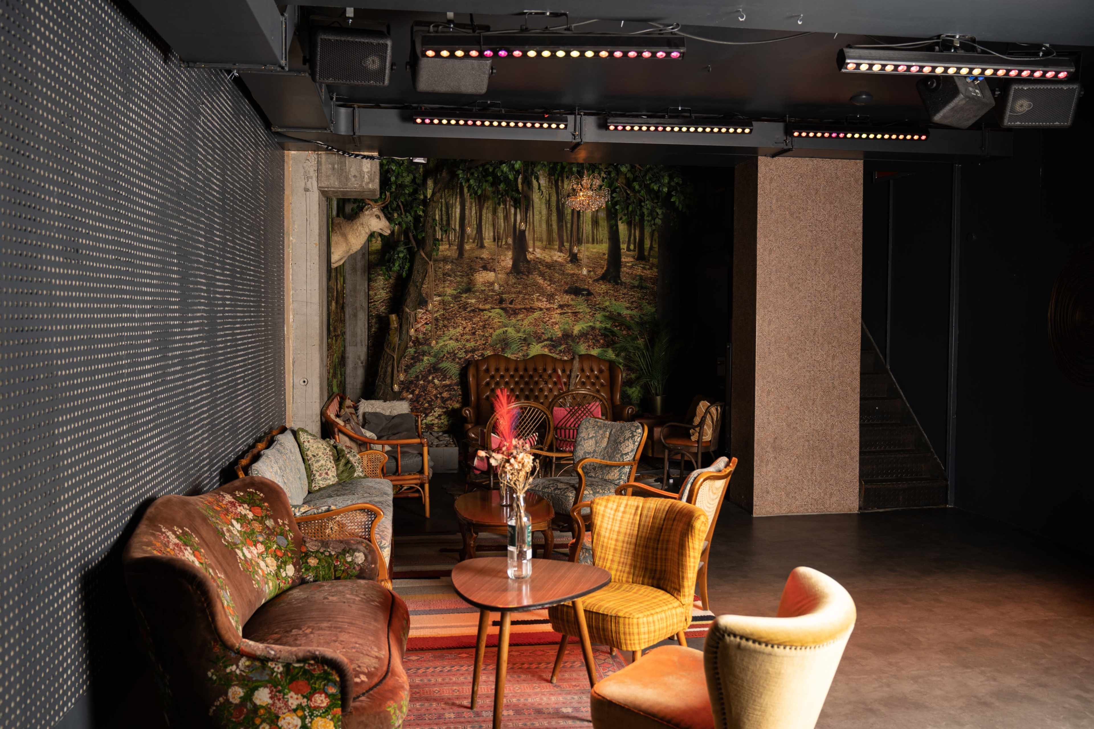The image shows a cozy lounge area with vintage furniture and a forest-themed mural on the wall.