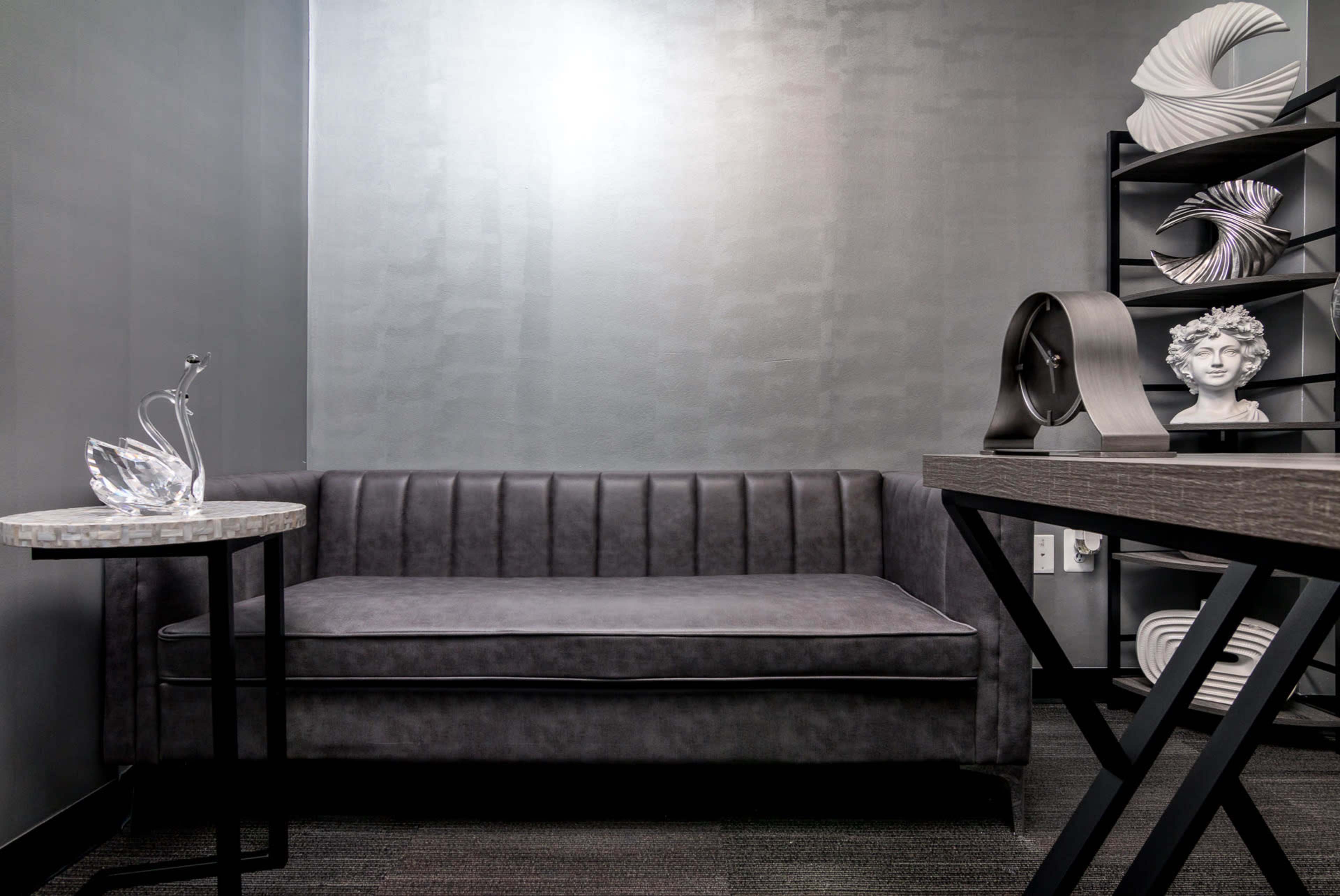 A modern seating area featuring a gray couch, a decorative table with a crystal sculpture, and a shelf displaying various artistic objects.