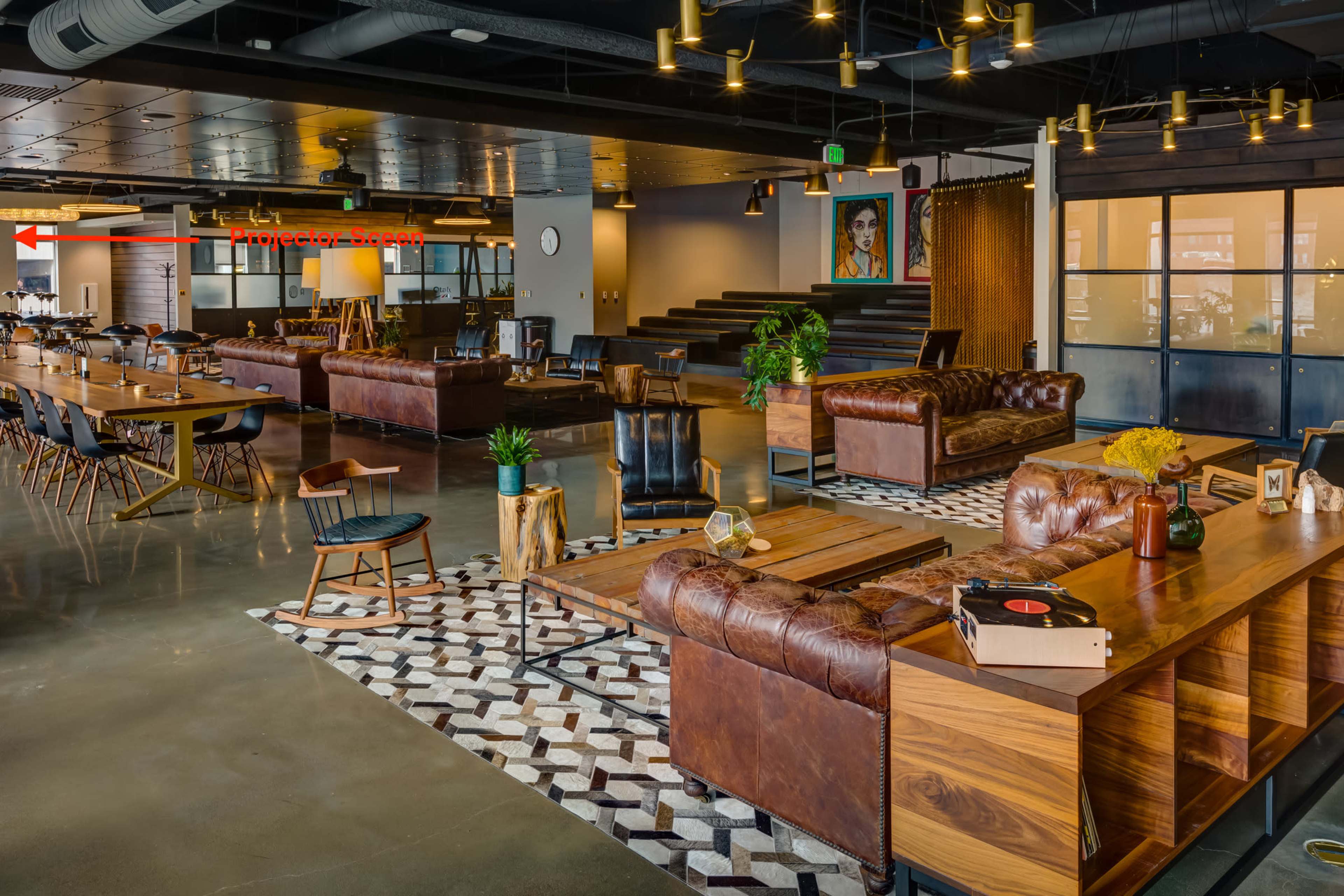 A modern office interior with leather sofas, wooden tables, and a patterned rug, featuring an open layout and decorative lighting.
