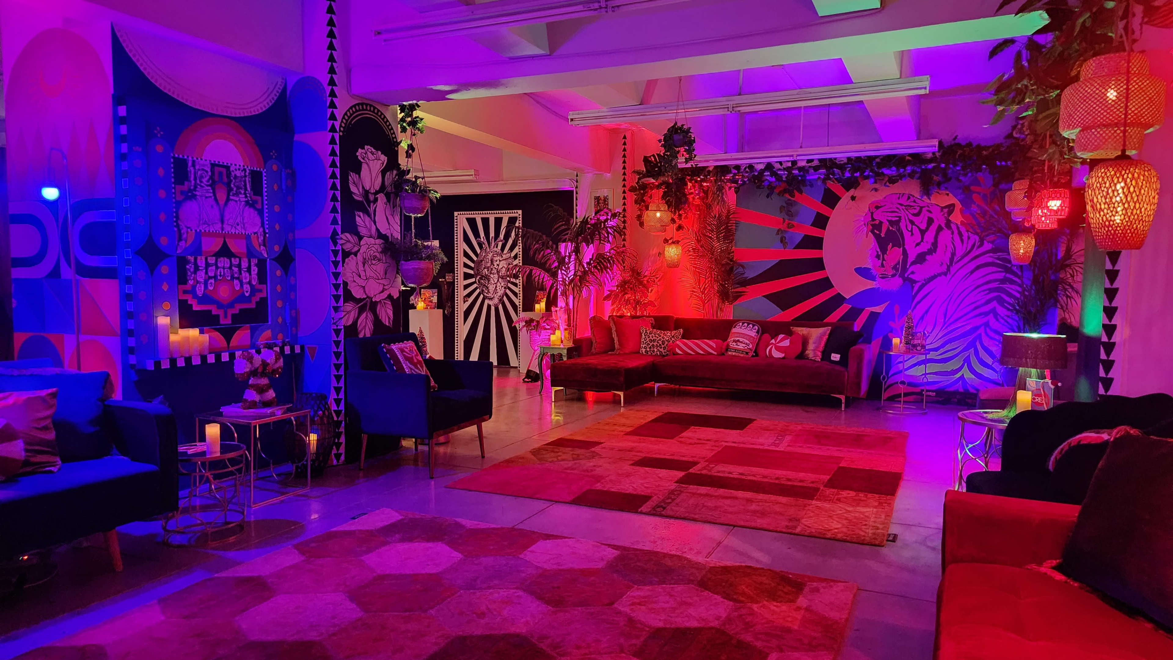 The image features a vibrant and colorful lounge area with bold wall art, mixed seating arrangements, and decorative lighting in a modern interior space.