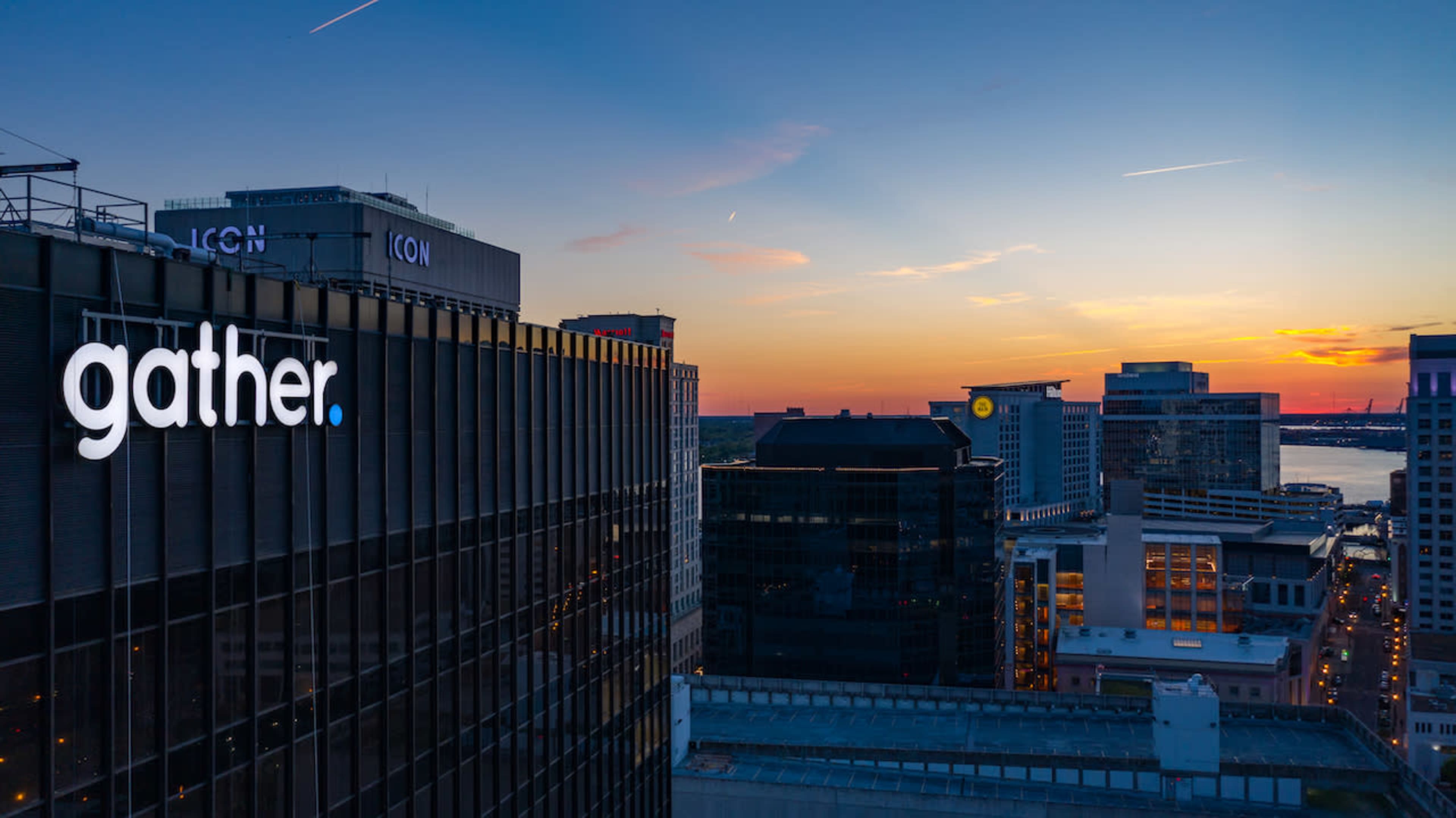 The image shows a skyline at sunset with the word "gather" illuminated on a building.