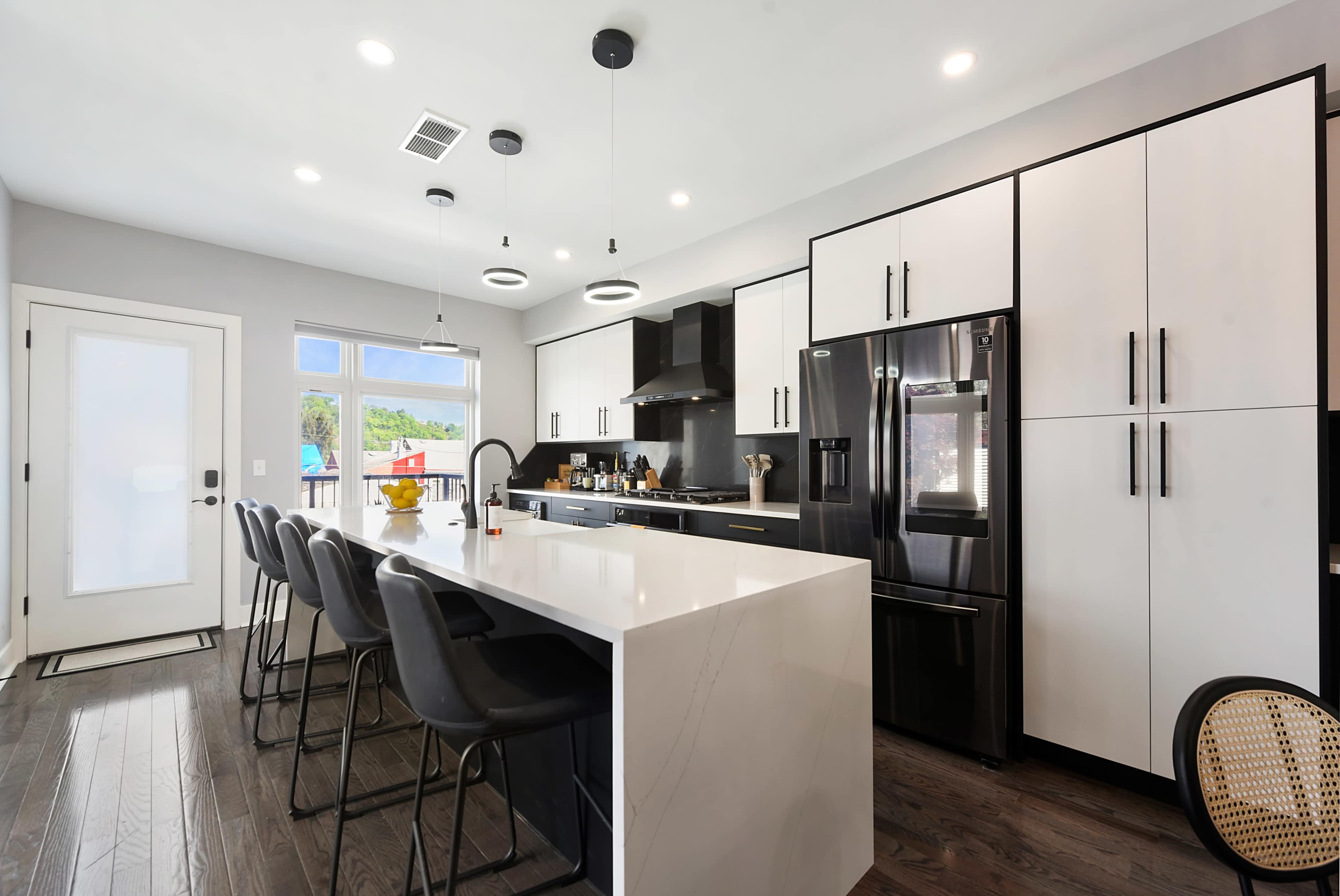 A modern kitchen featuring a large island with seating, black and white cabinetry, and stainless steel appliances.