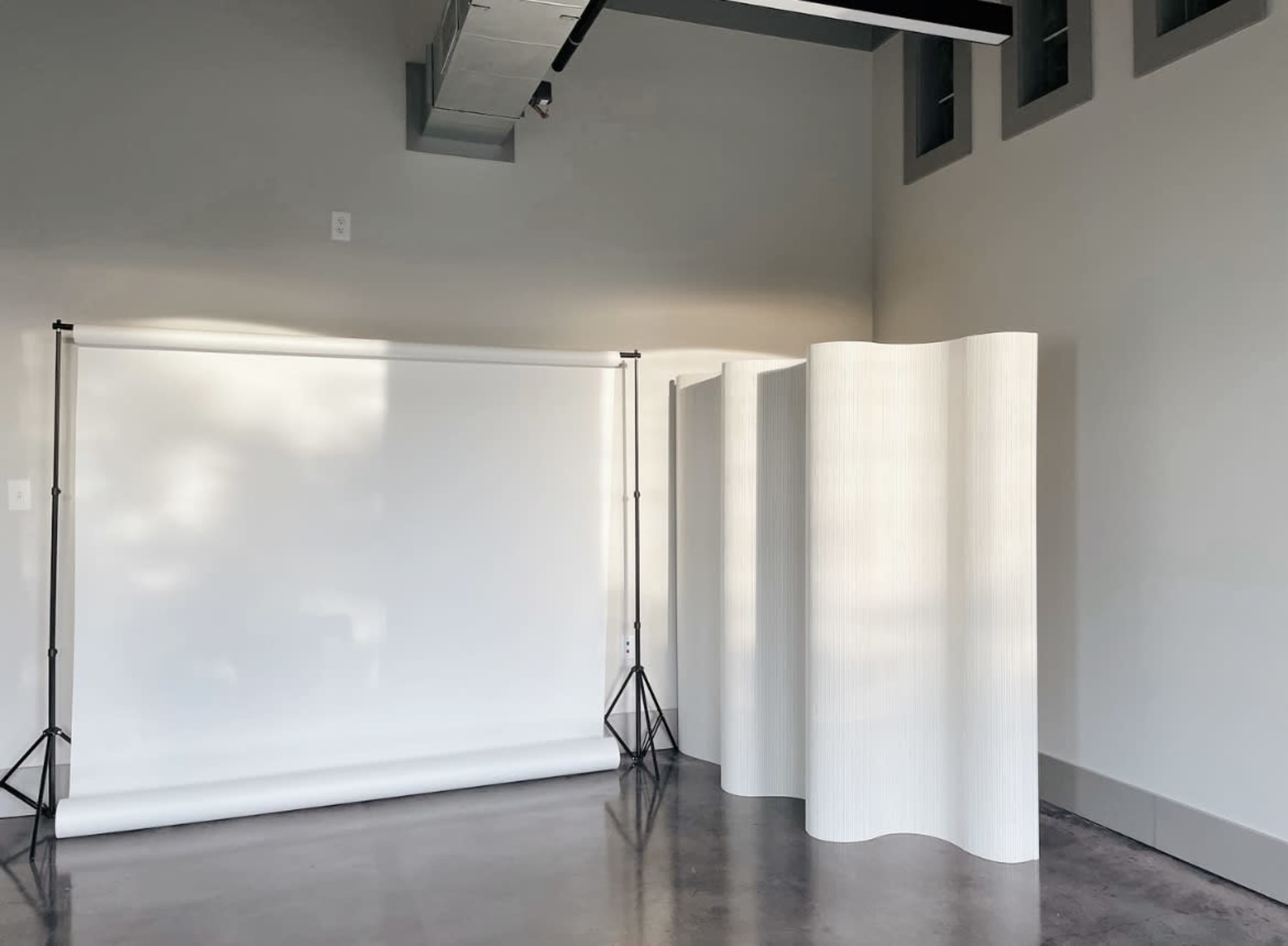 A spacious interior featuring a photography backdrop setup with a white roll and two curved white dividers against a gray wall.