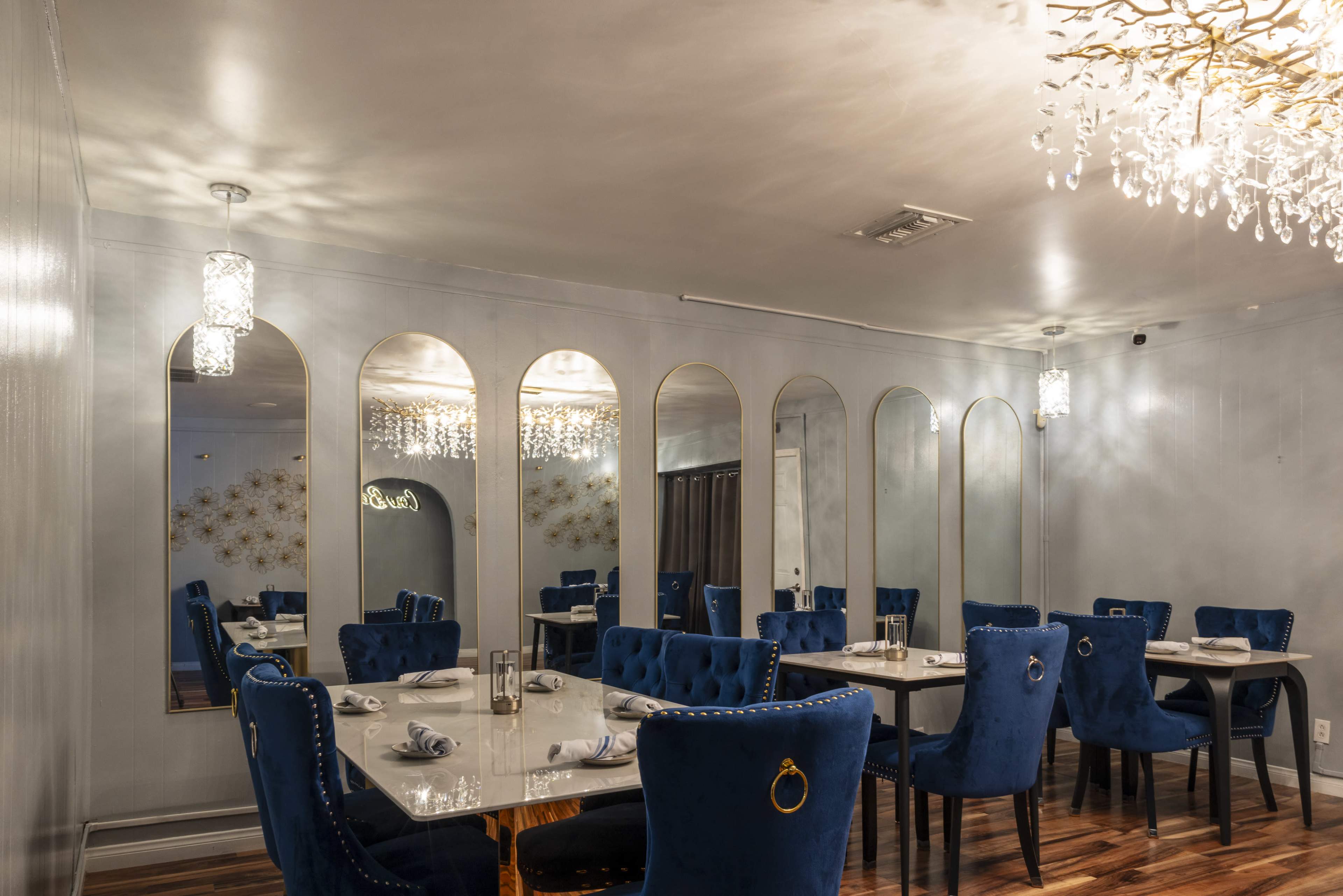 The image shows a modern restaurant interior with blue velvet chairs around tables, mirrored walls, and elegant lighting fixtures.