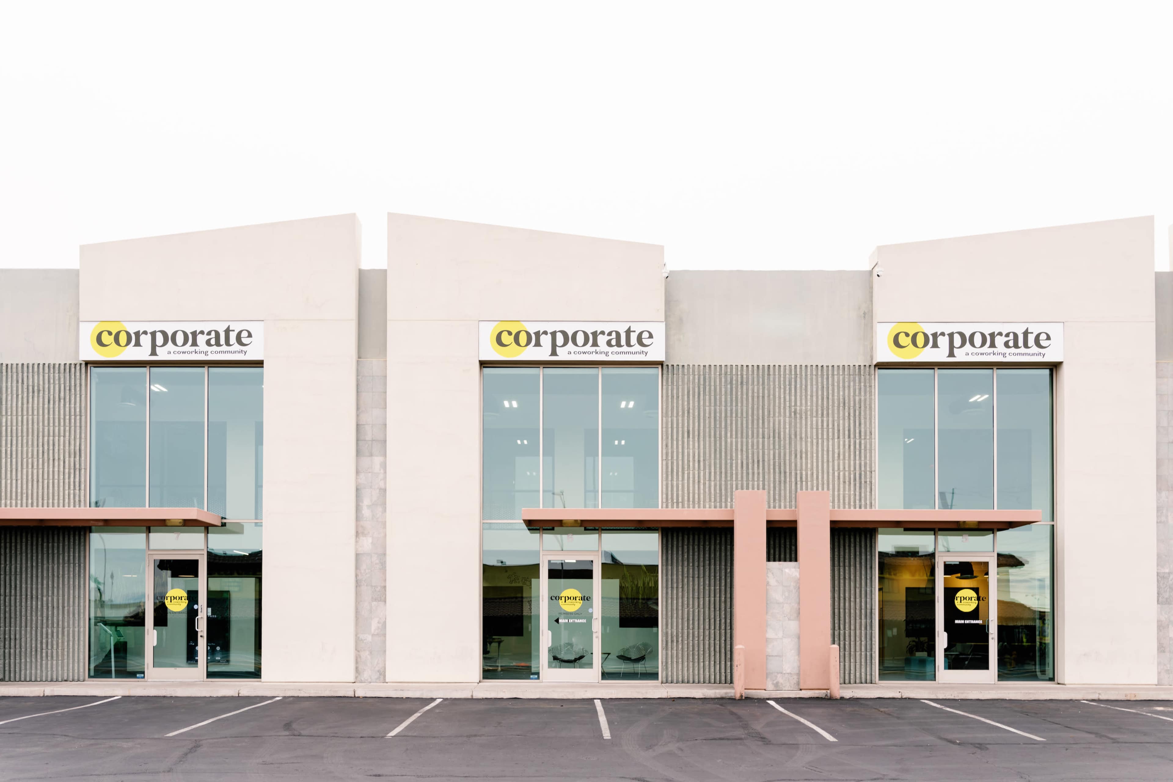 The image shows a modern commercial building with three identical storefronts, each featuring large glass windows and signage above the entrances.