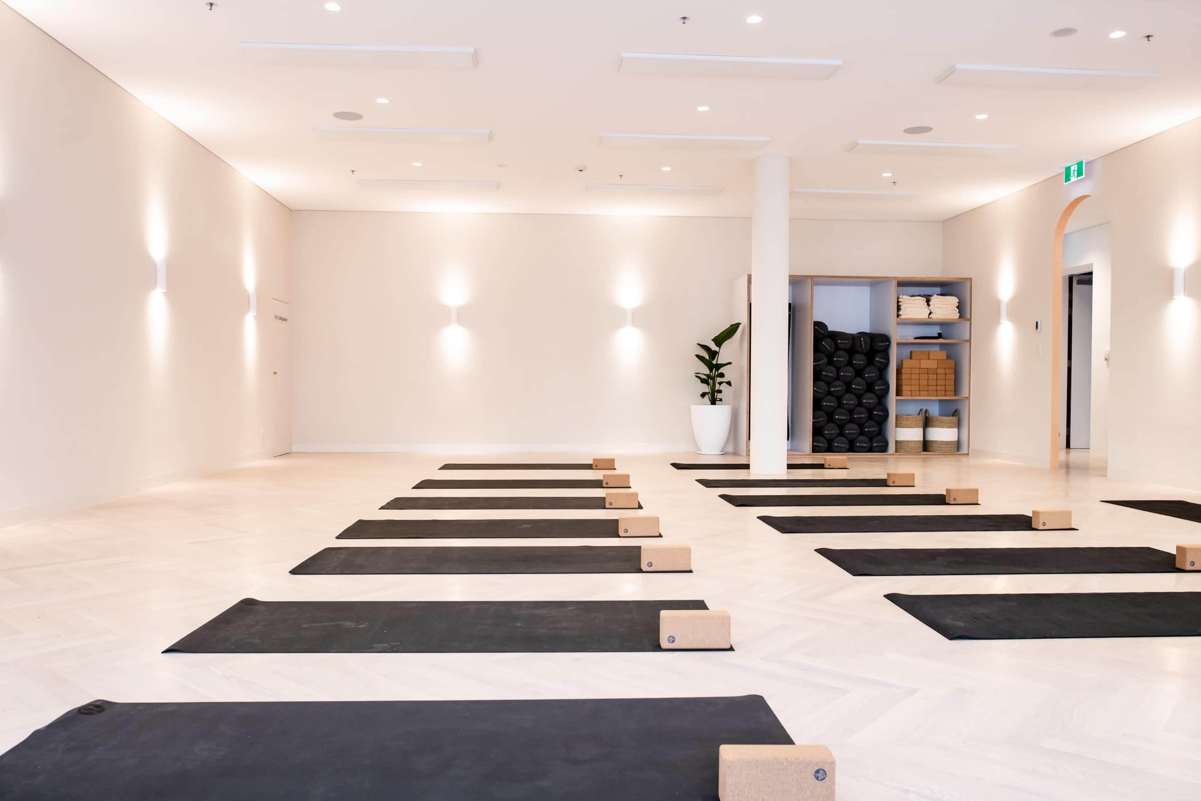 A yoga studio with neatly arranged black mats, cork blocks, and a shelf of rolled mats, illuminated by soft overhead lighting.