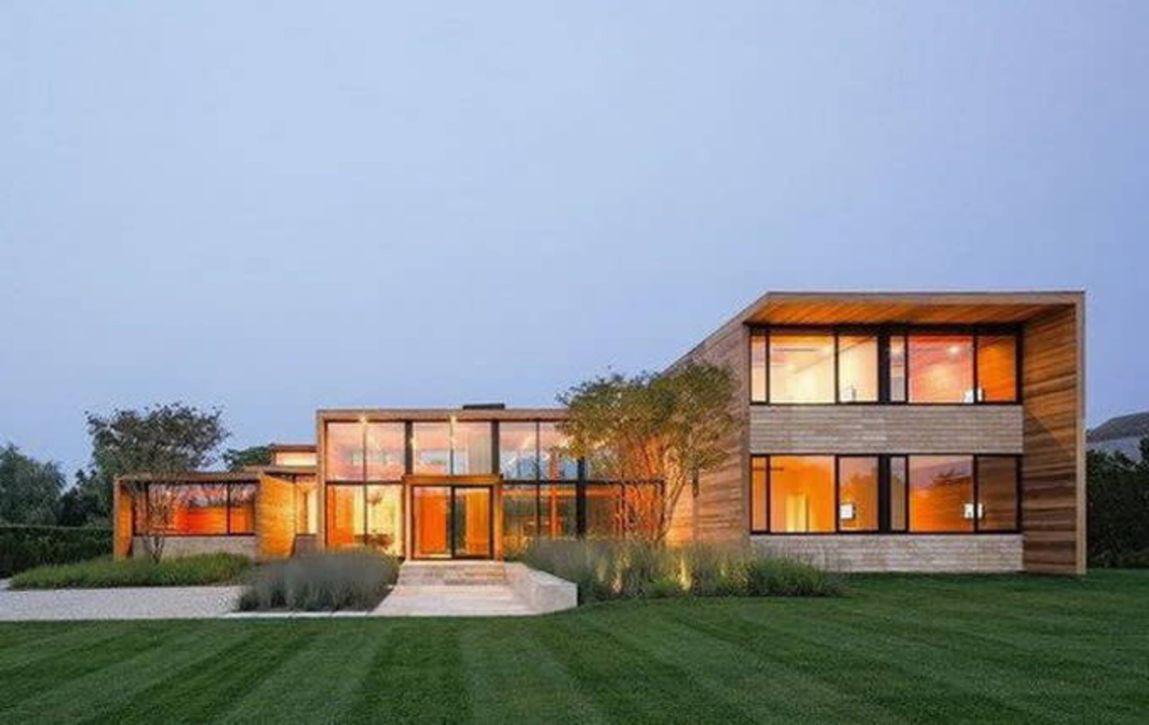 A modern house features large glass windows, wooden accents, and a neatly landscaped yard.
