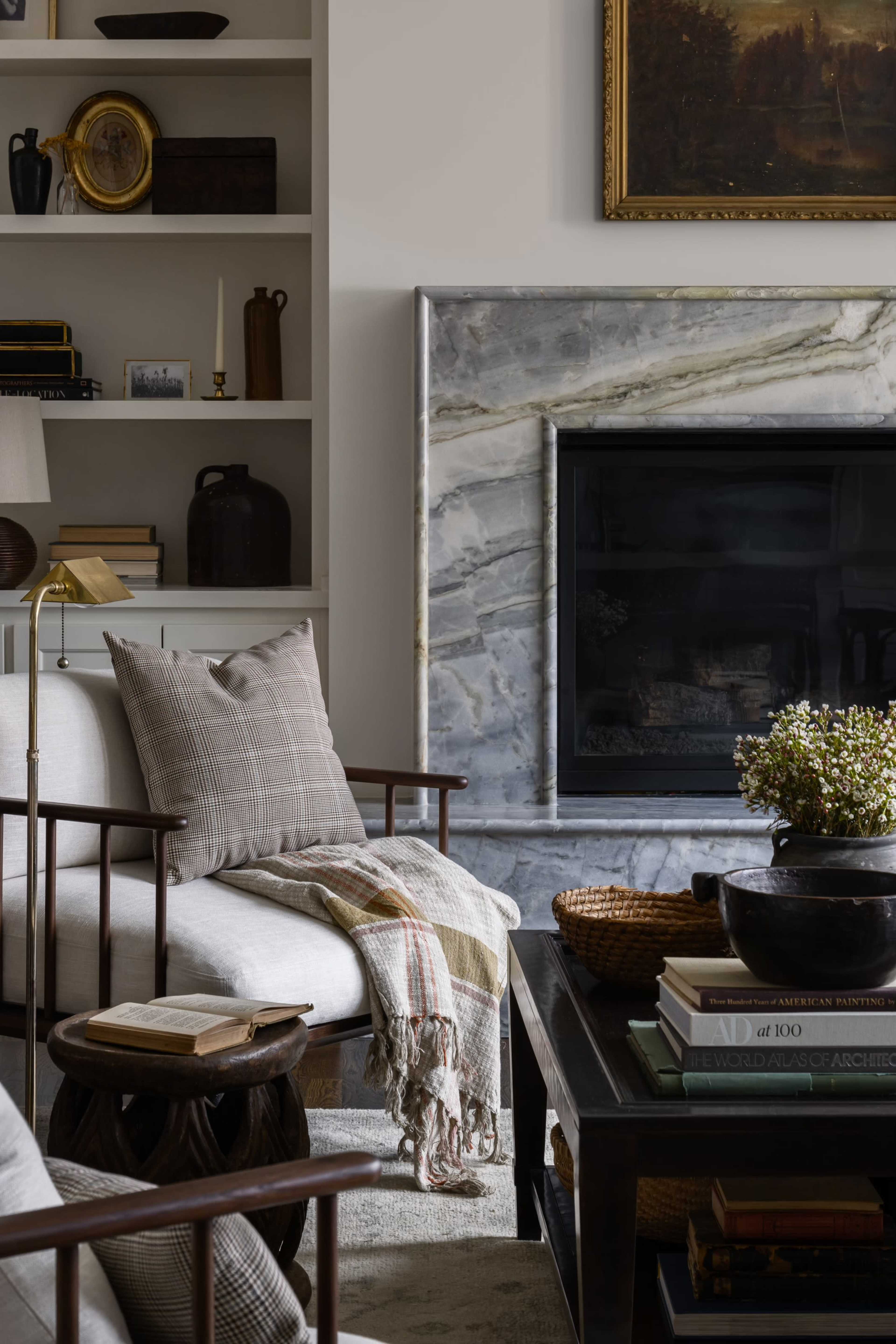 A cozy living room features a marble fireplace, bookshelves with decor, and comfortable seating adorned with a throw blanket.