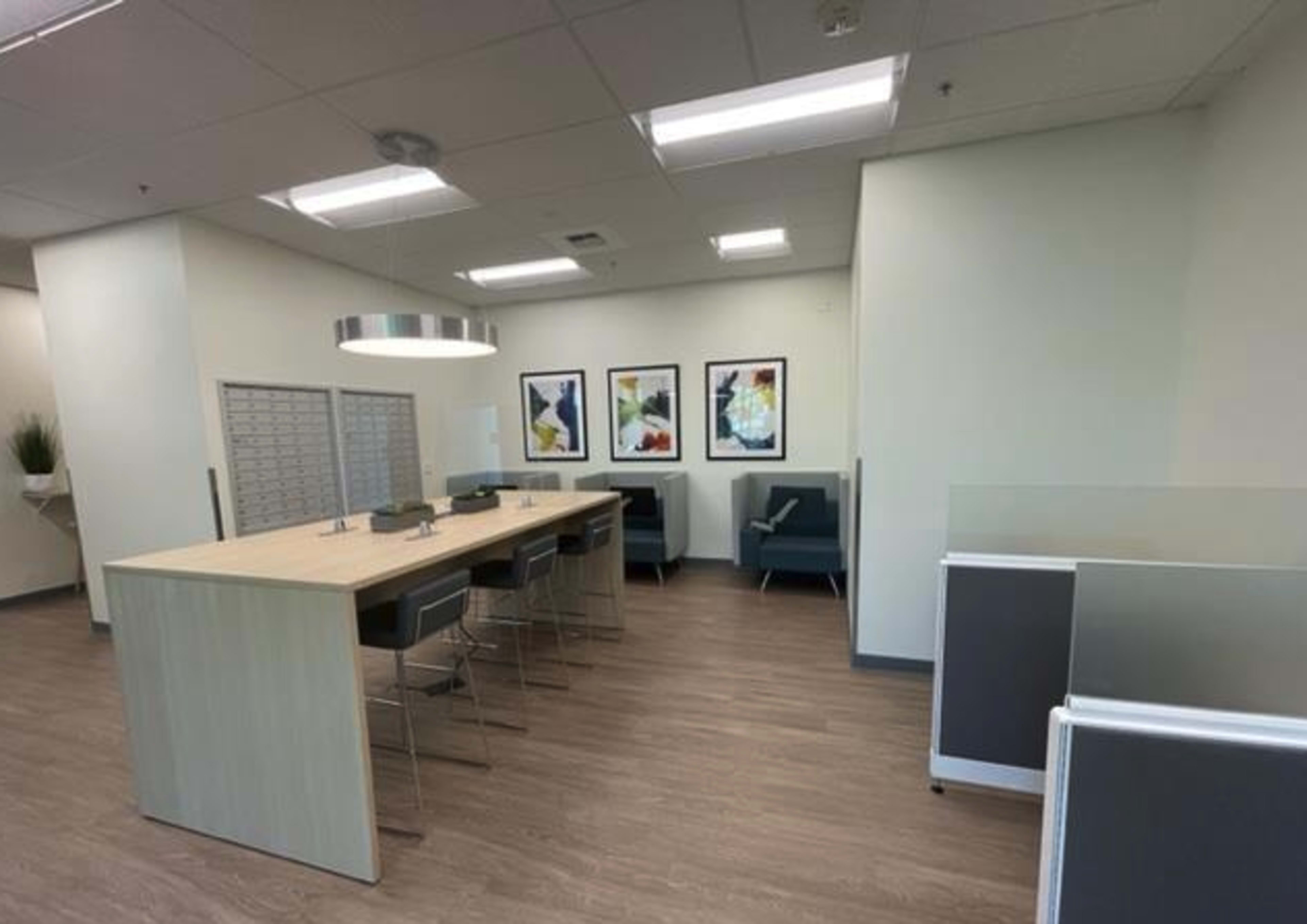 A modern office space featuring a long table with chairs, a sofa area, and framed artworks on the walls.