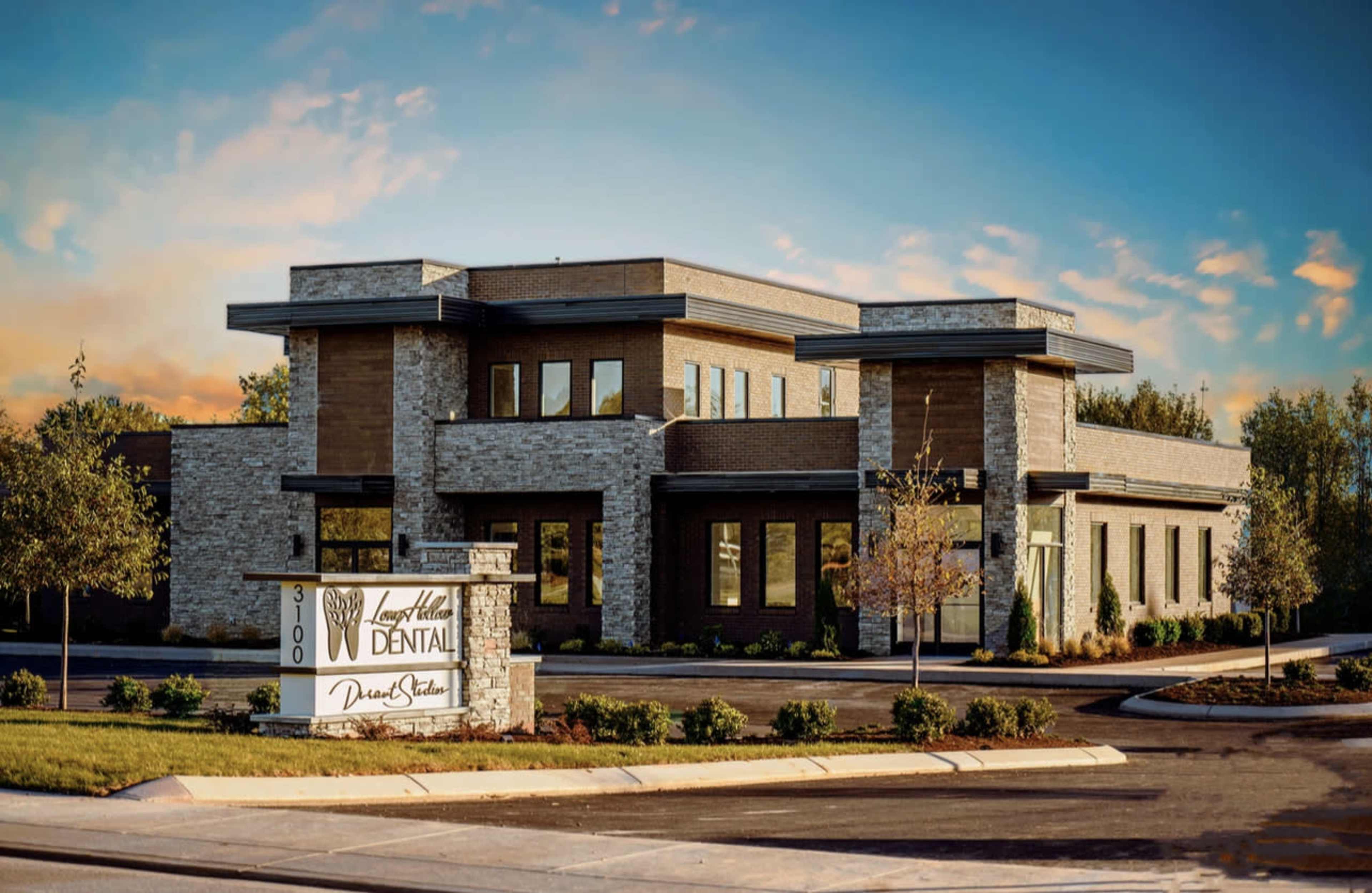 A modern dental office building featuring stone and wood accents with a prominent sign in the foreground.