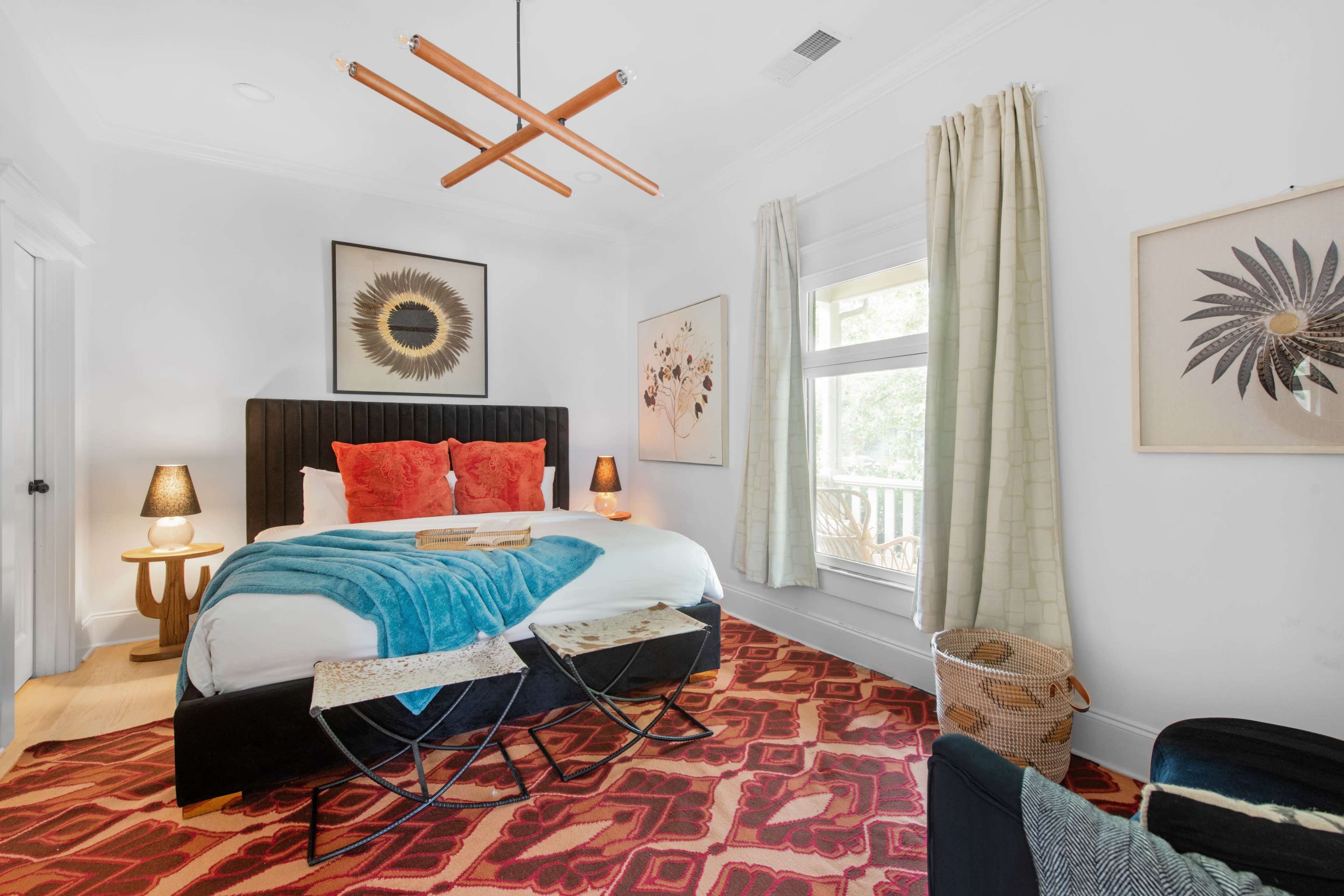 A modern bedroom features a bed with a geometric headboard, decorative pillows, and a patterned rug, accompanied by artwork and a stylish light fixture.