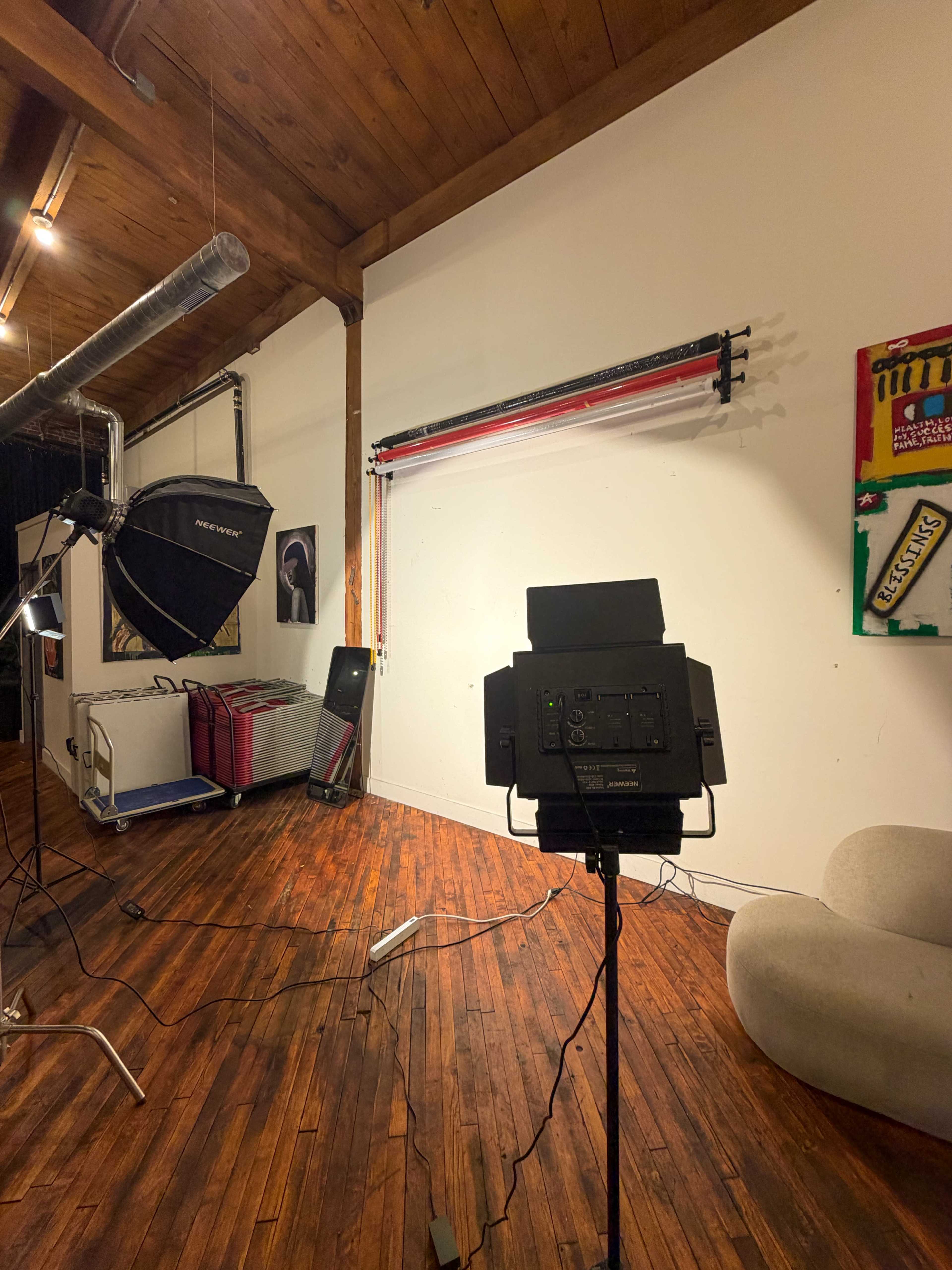The image shows a photography studio setup with a lighting equipment, a backdrop, and a comfortable chair against a wooden floor and wall.